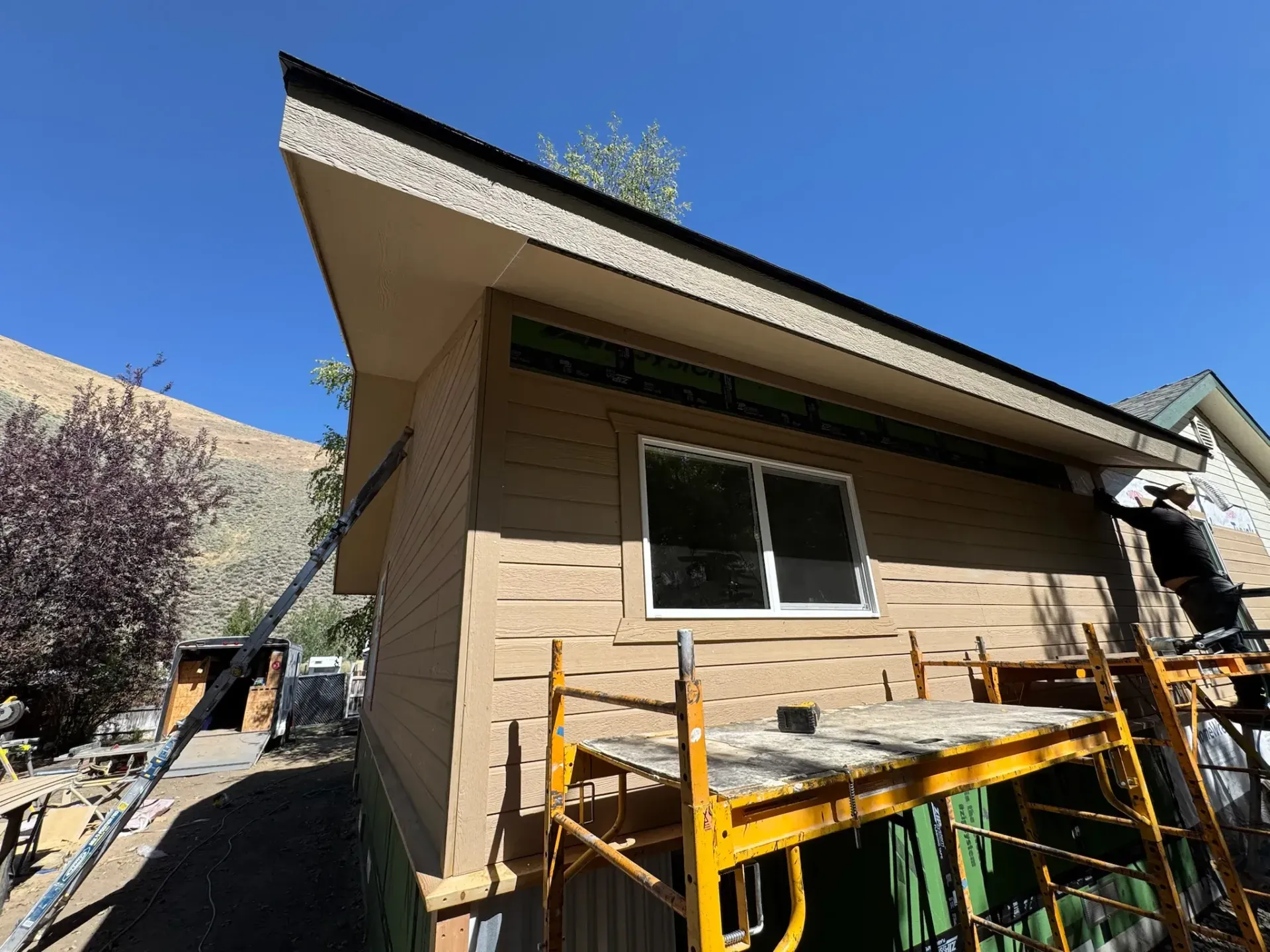 House exterior with slanted roof, beige siding, and construction scaffolding under a bright blue sky