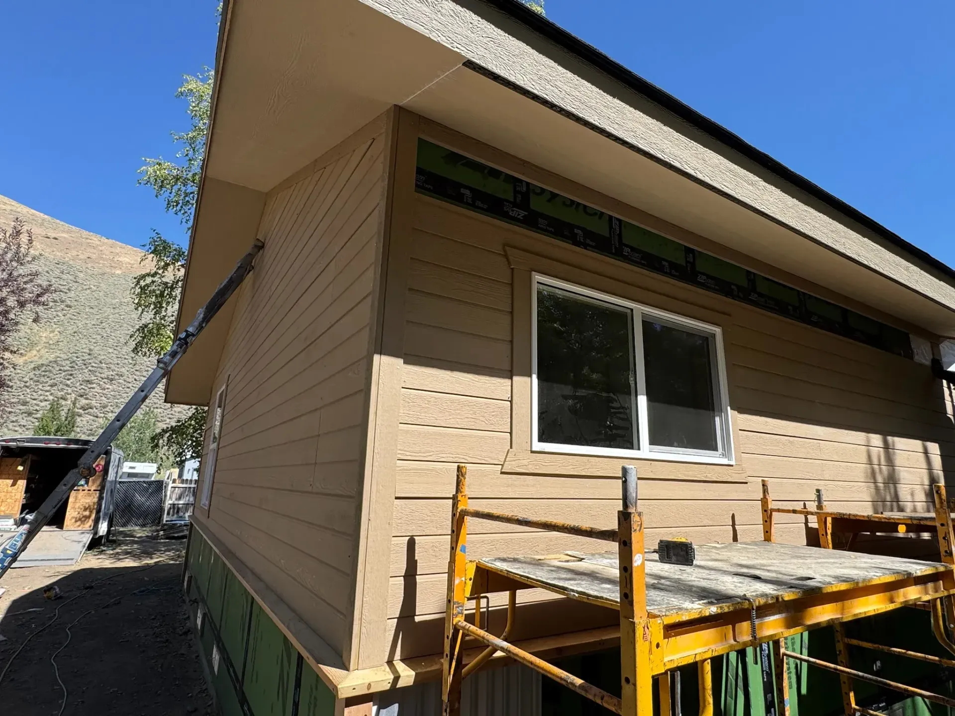 Tan house exterior with window and yellow scaffolding on a sunny day