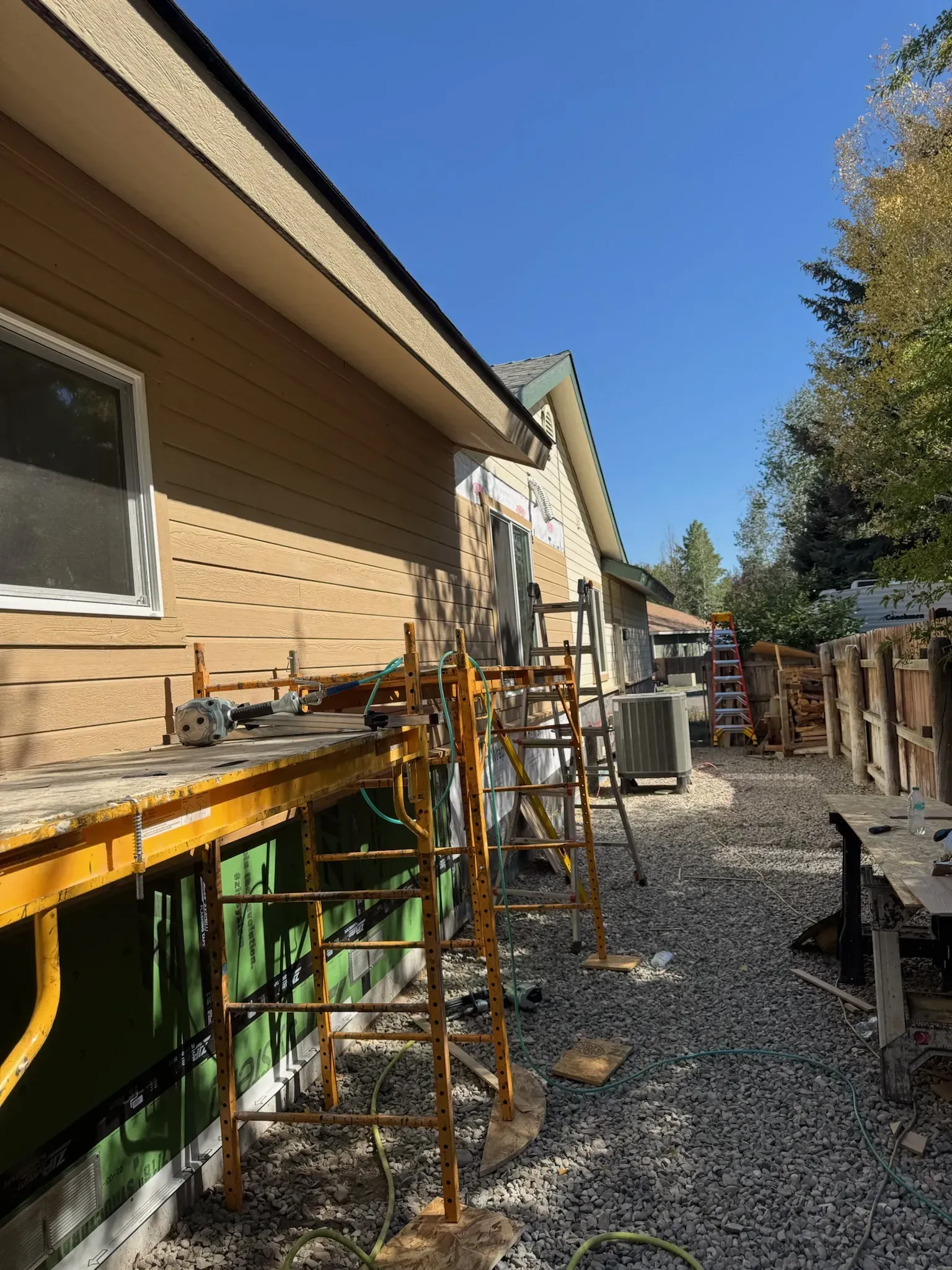House exterior with scaffolding and construction tools beside a gravel walkway under a clear blue sky