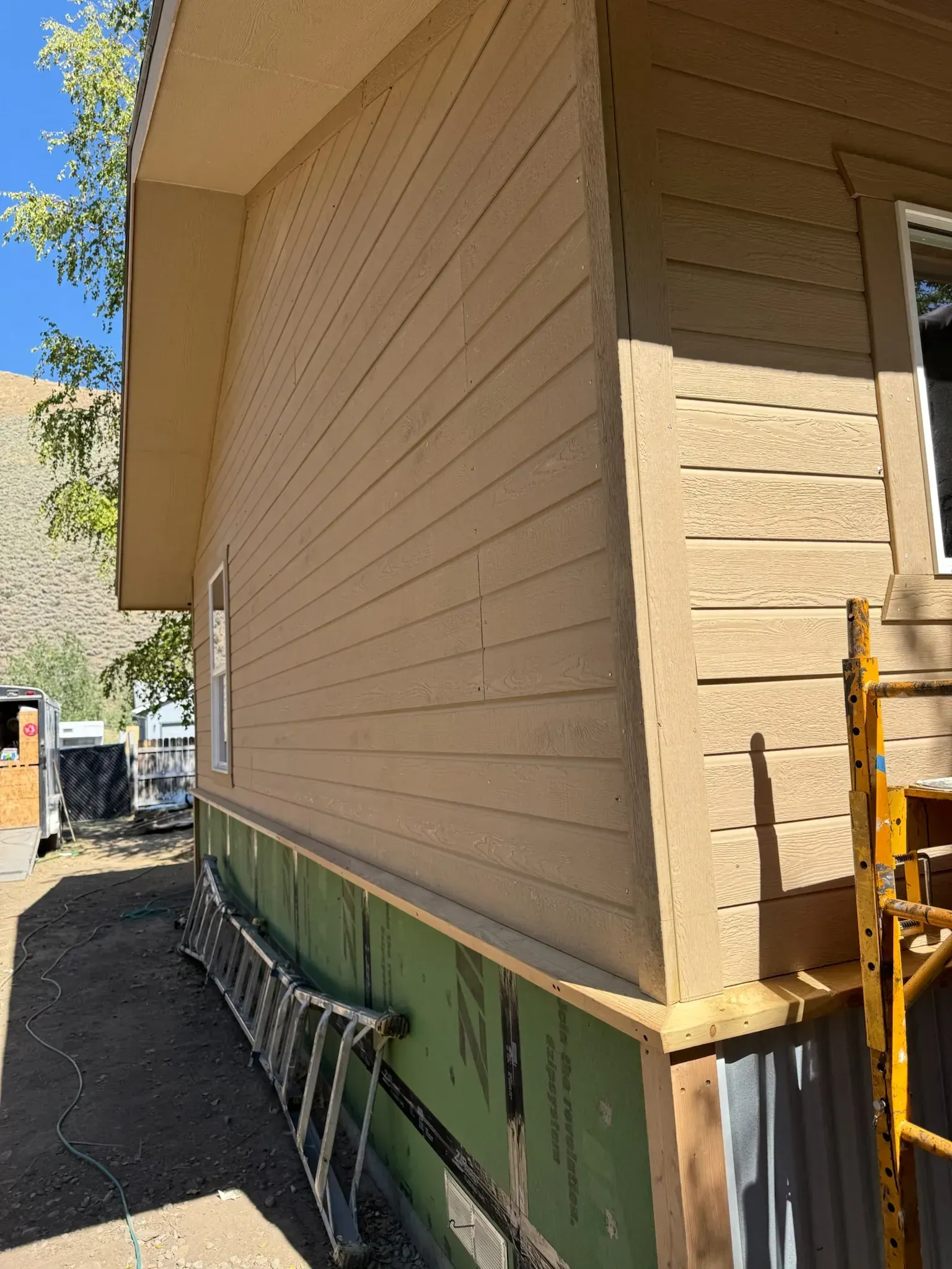 Side view of a tan house with green trim, showing a ladder leaning against the exterior wall.