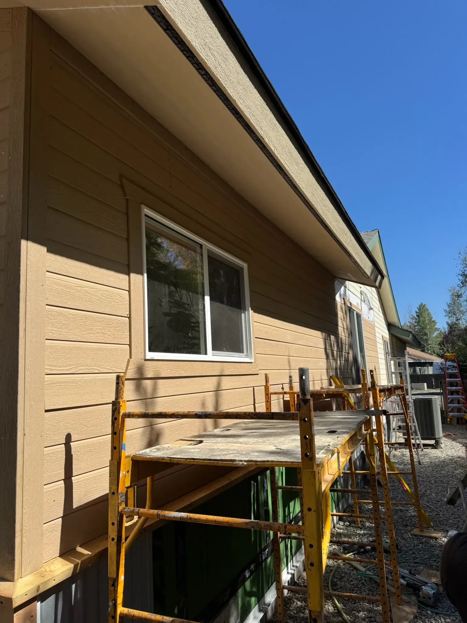 House exterior with a wooden deck under construction beside tan siding and a blue sky