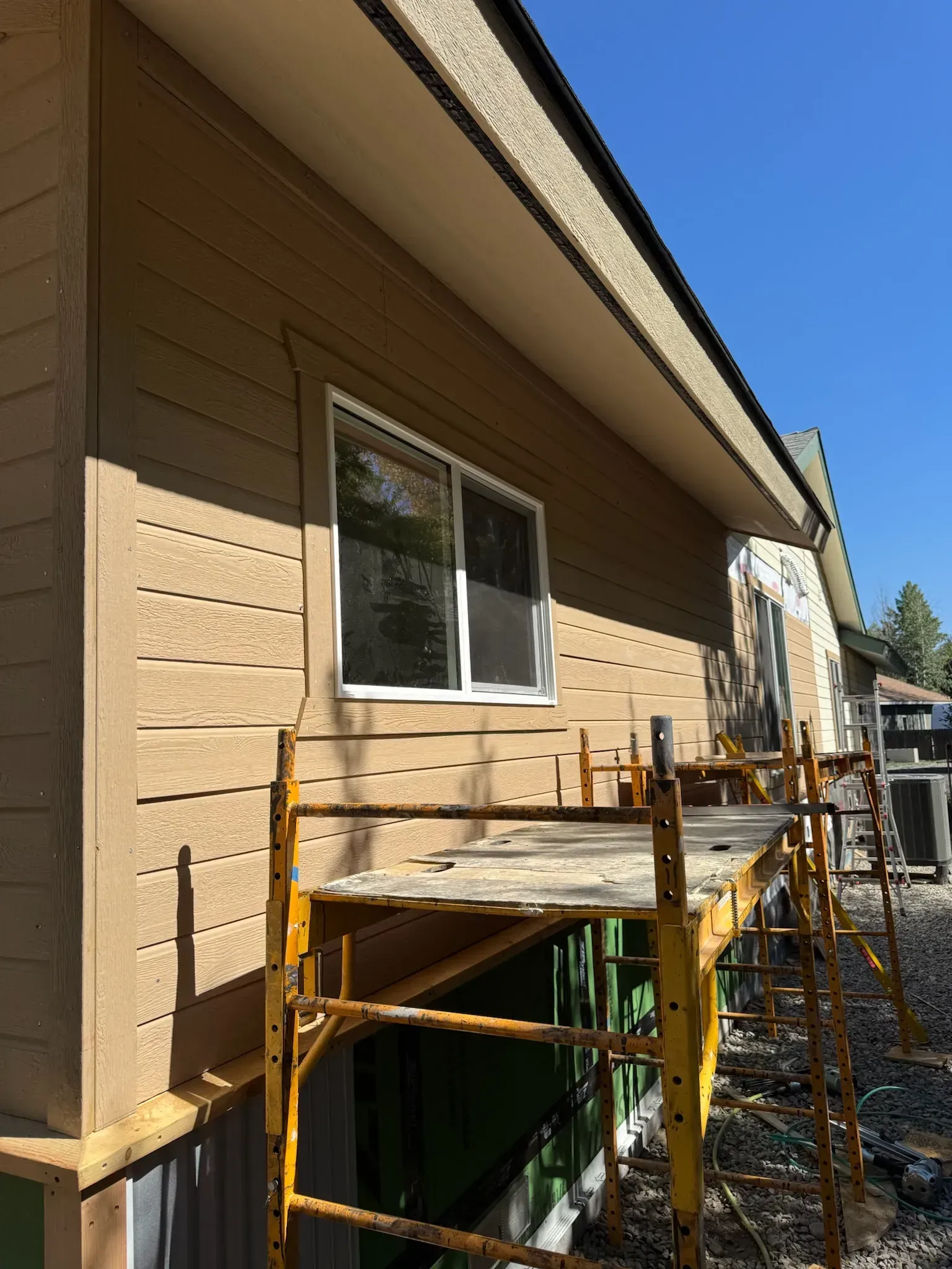 House exterior with tan siding and a window, showing construction scaffolding along the side wall.