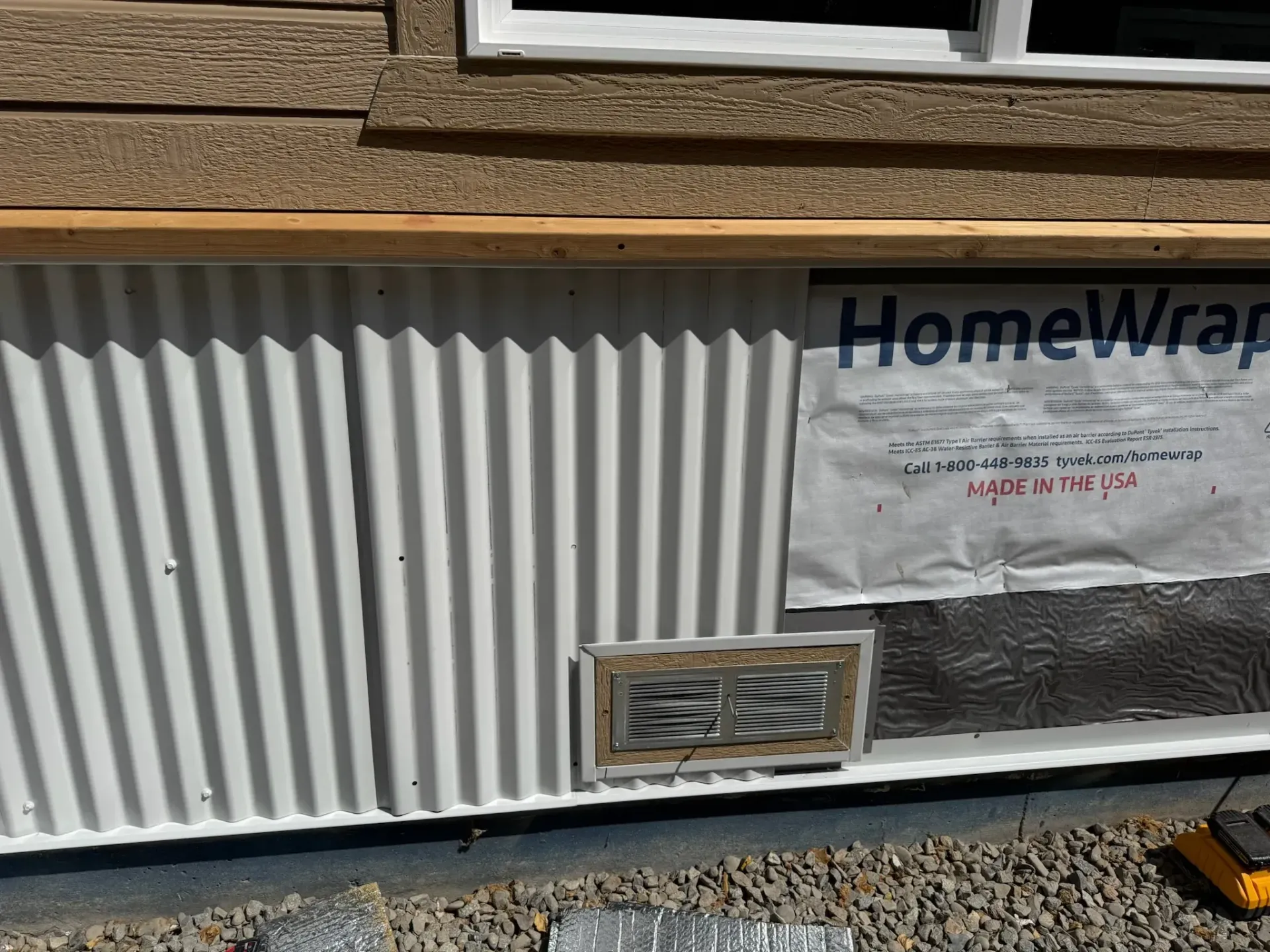 House exterior with corrugated siding, a window, and a HomeWrap wrap panel under construction
