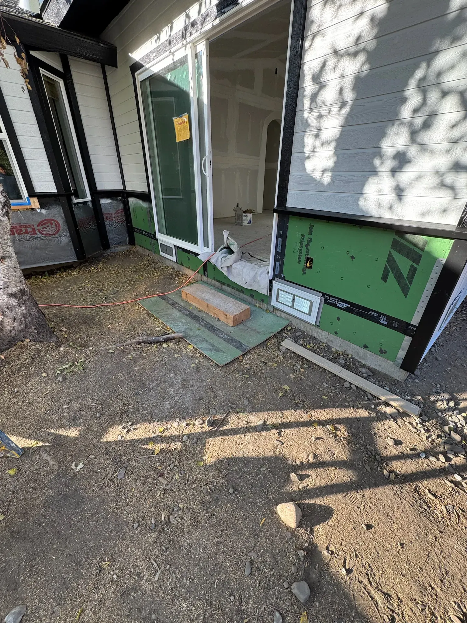 Partially open green front door with a small step, gravel yard, and house siding in daylight
