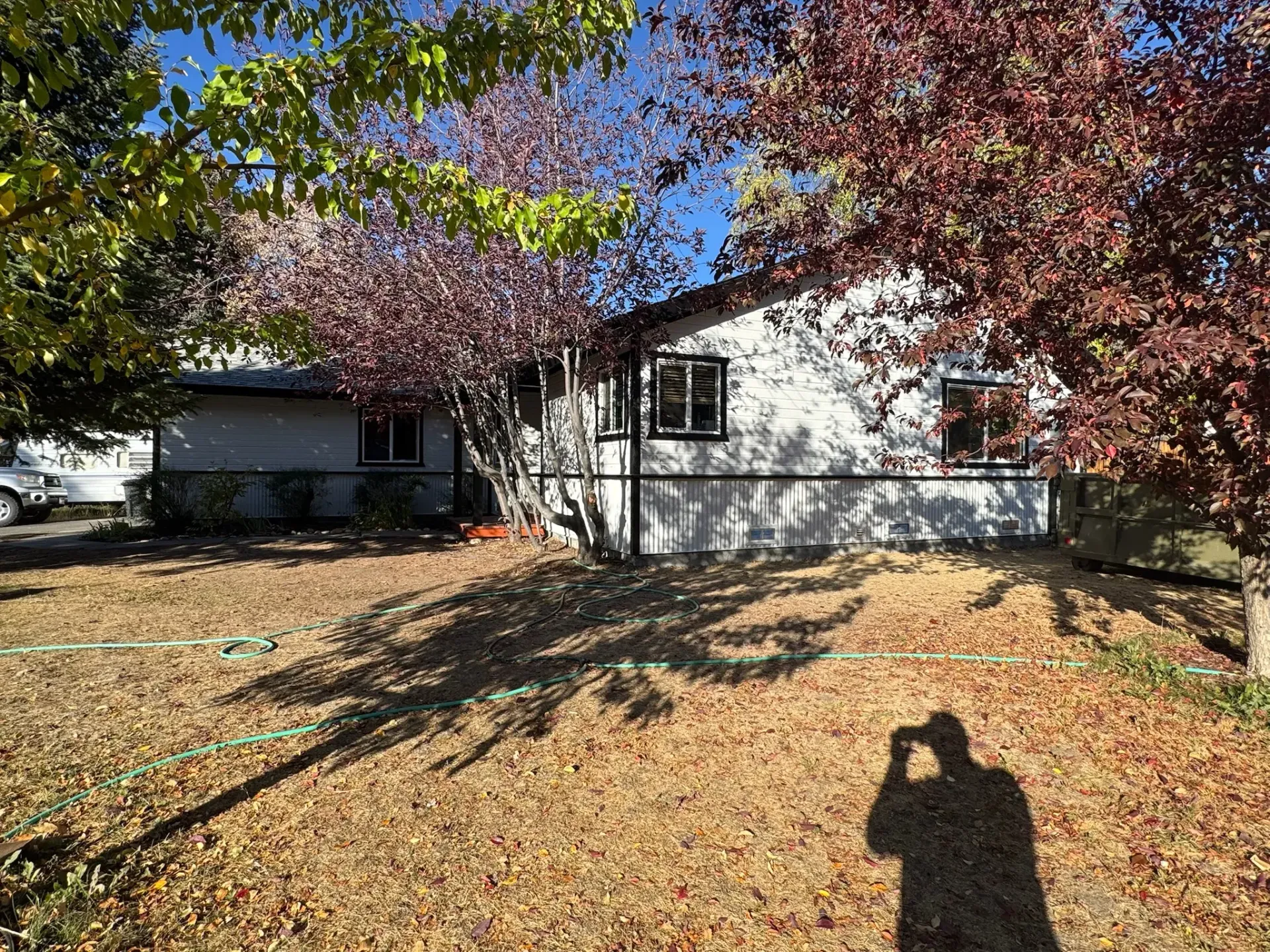 Suburban house with white siding, autumn leaves, and a long photographer’s shadow in the yard