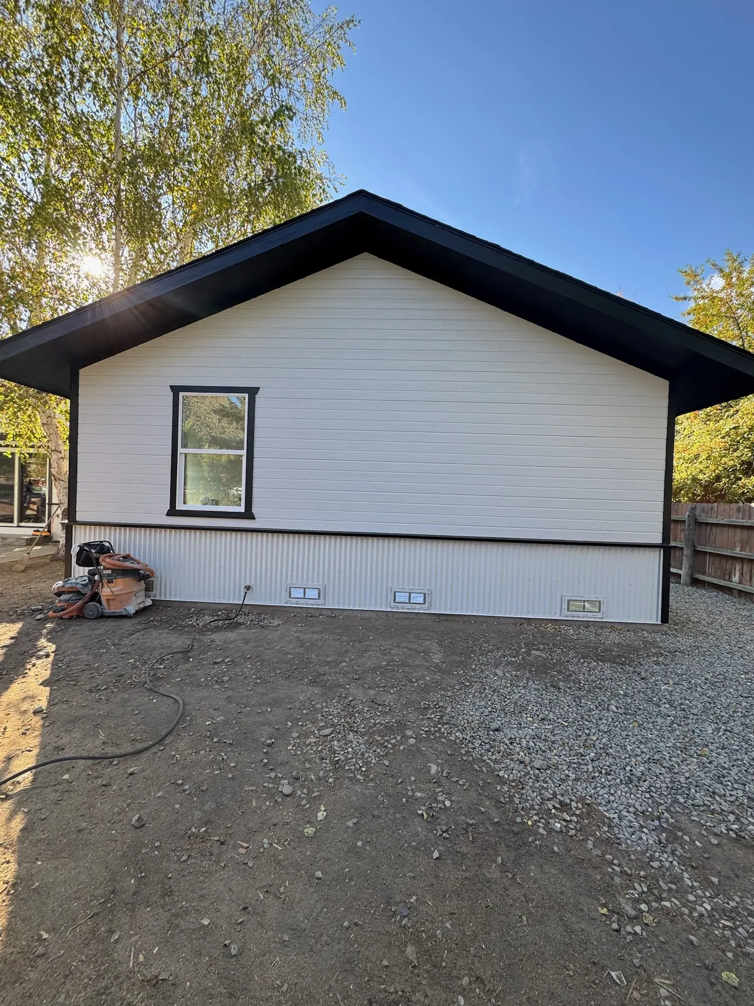 Side view of a small white house with black trim and a gravel driveway under a clear blue sky