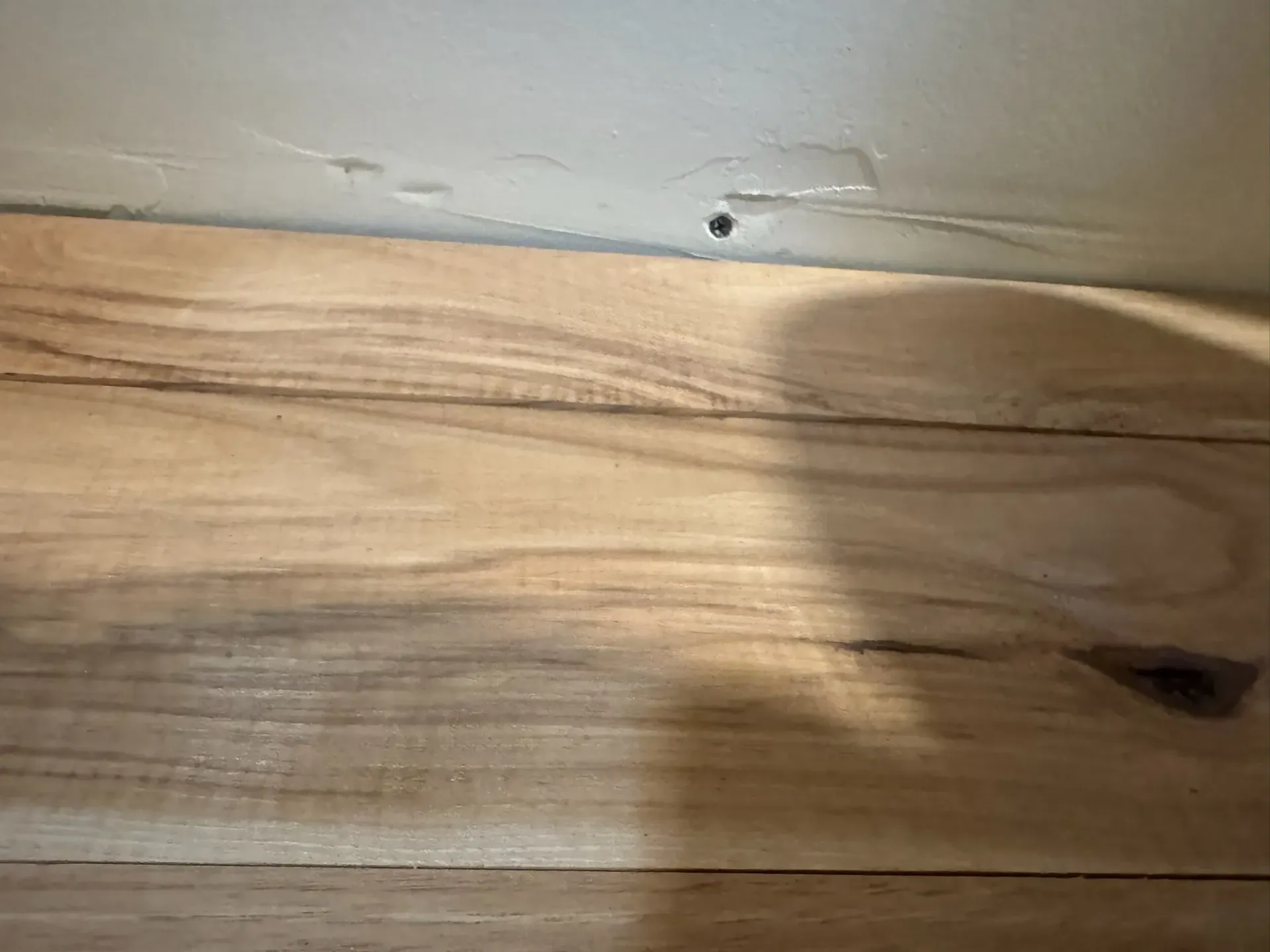 Close-up of a light wood tabletop with a small dark knot and shadow across the surface