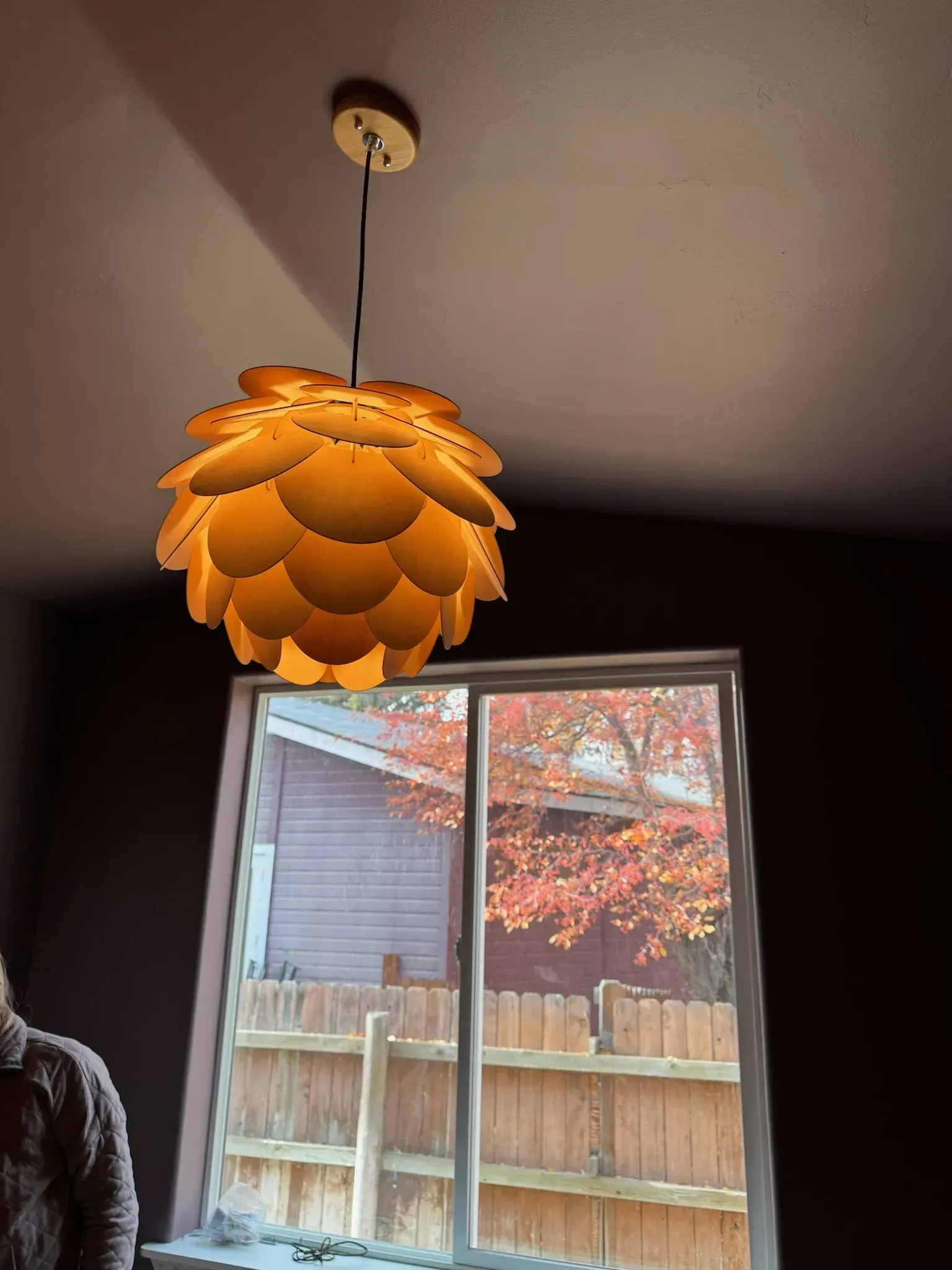 Orange pendant lamp with layered petals hanging above a window in a dim room