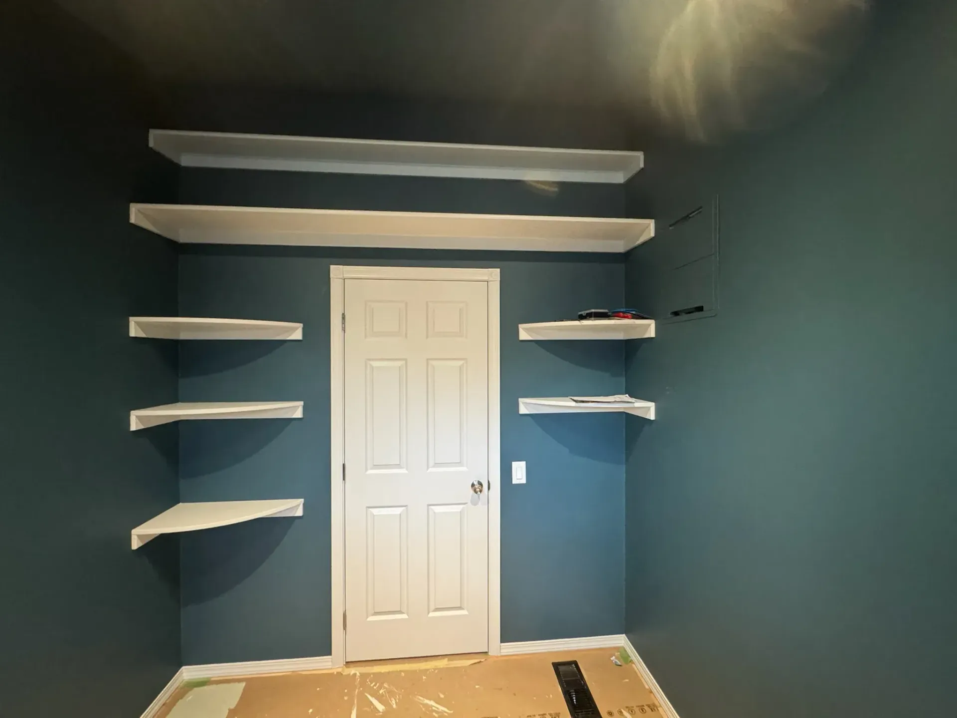Blue room with white floating shelves and a white door centered on the back wall.