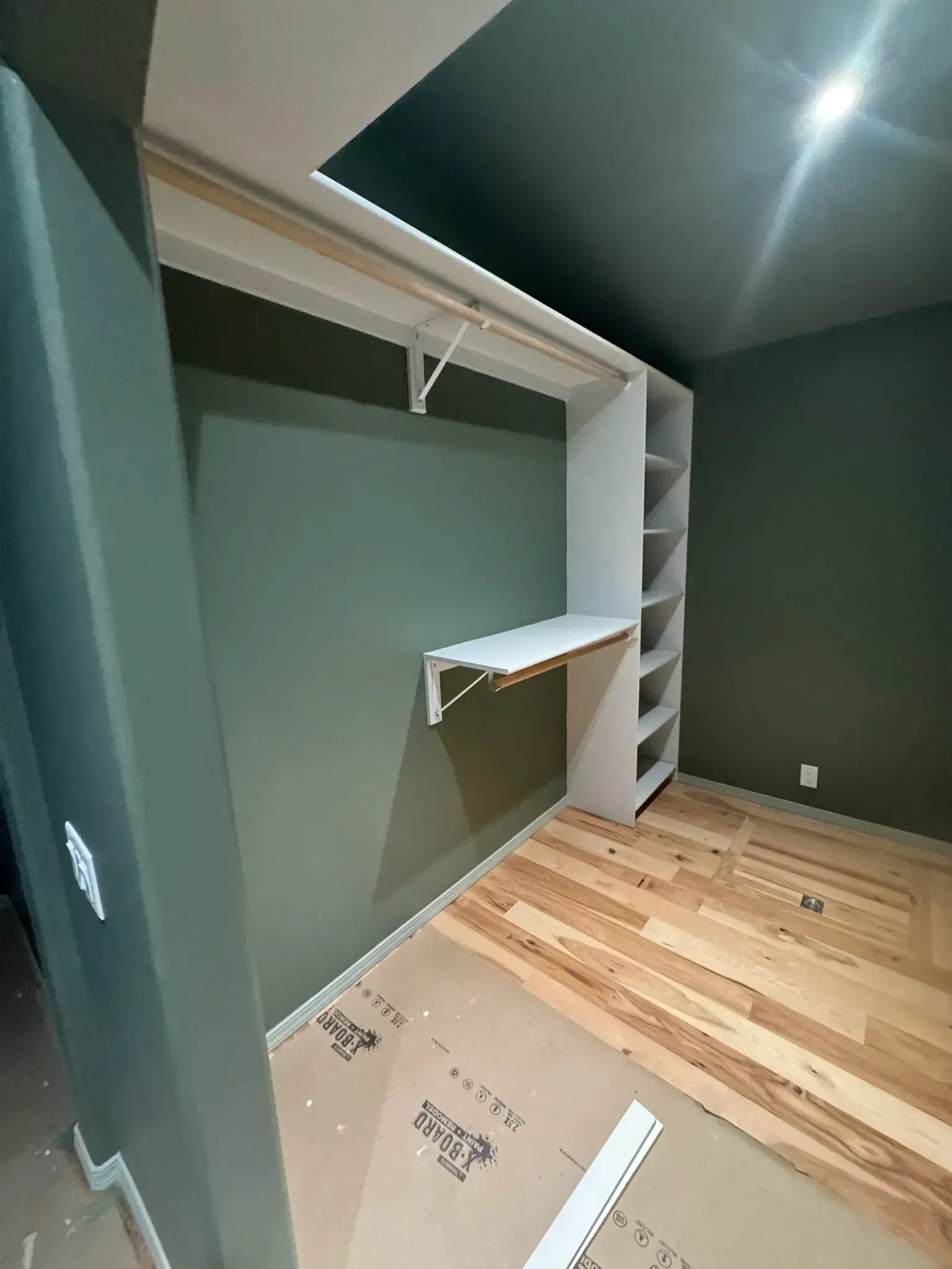 Small walk-in closet with green walls, white shelving, and light wood flooring.