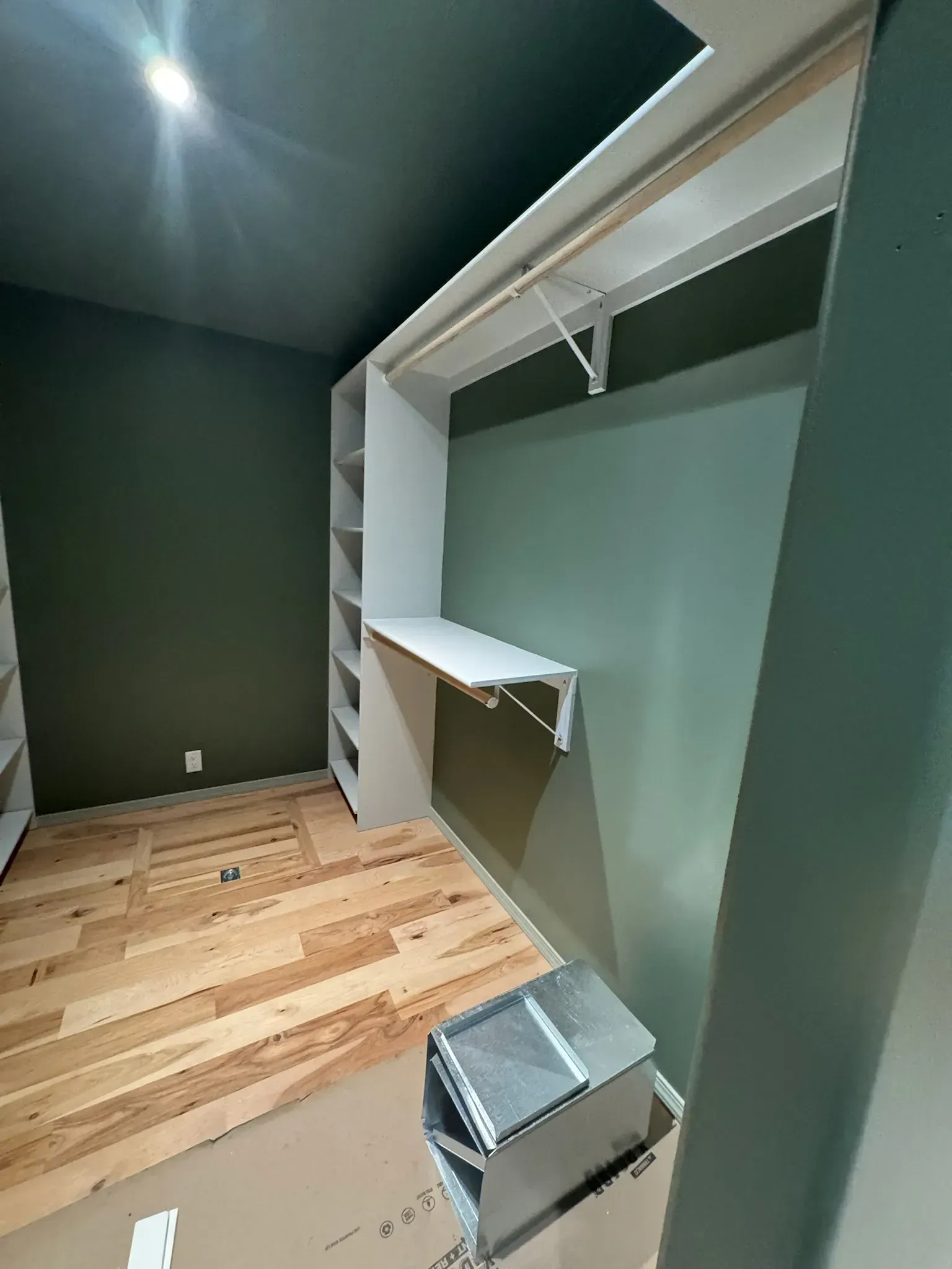 Empty walk-in closet with built-in white shelves, hanging rods, green walls, and hardwood floor.