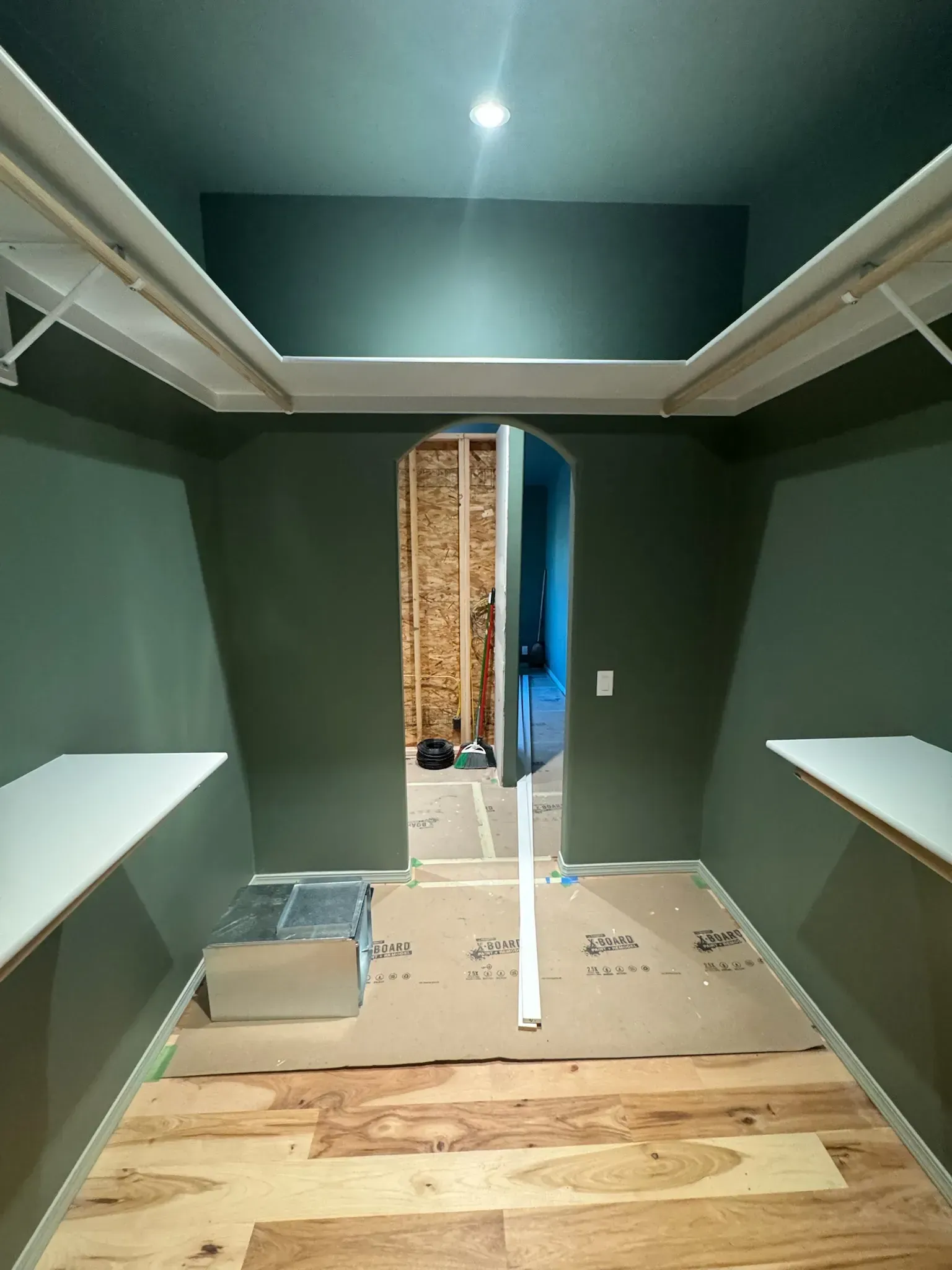 Empty walk-in closet under construction with green walls, white shelves, and unfinished floor.