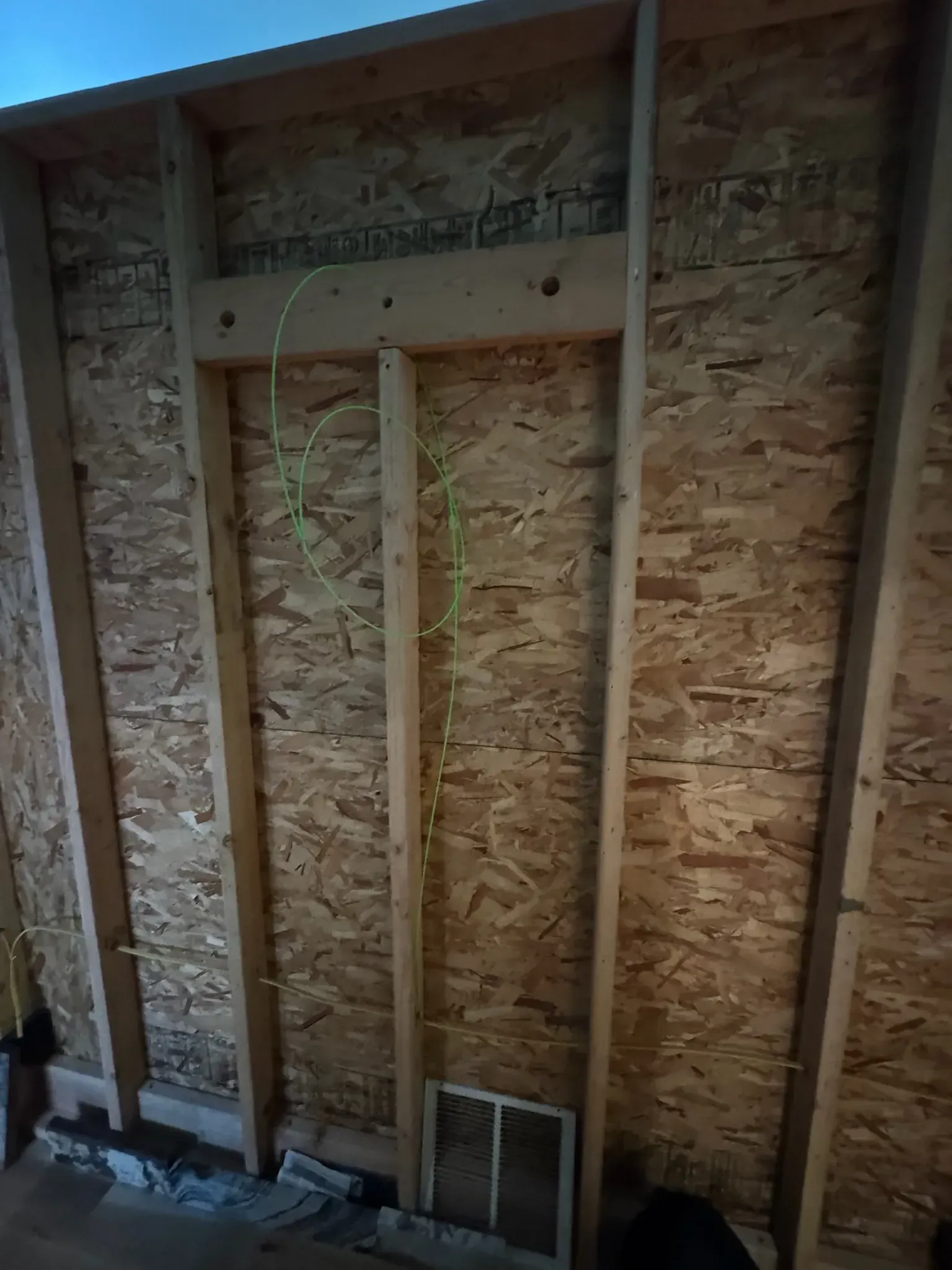 Exposed wood framing and OSB sheathing inside an unfinished wall, with a small vent opening near the floor