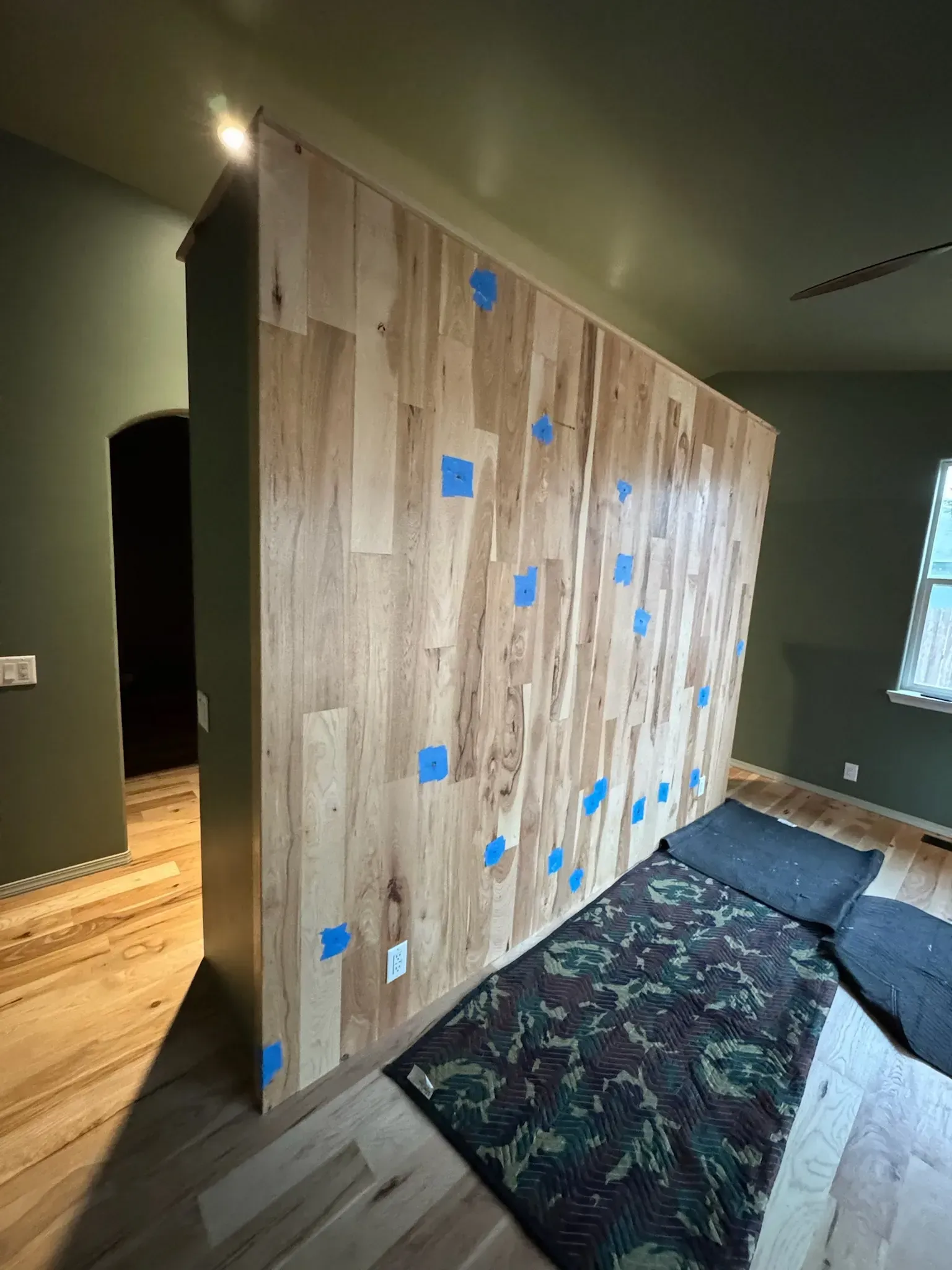 Wood-paneled partition wall with blue tape markers in a dark room, beside a carpet runner and window.