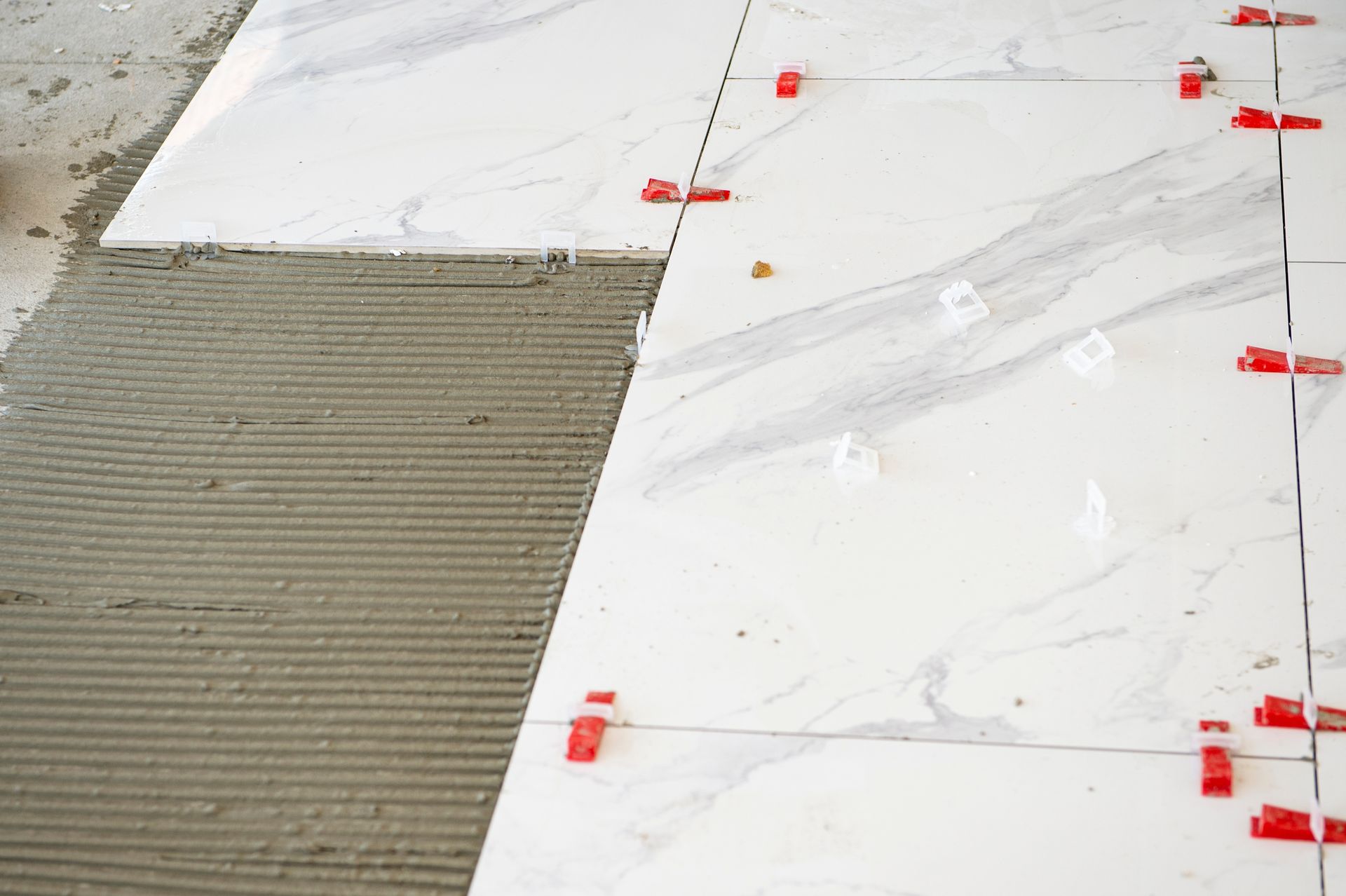 Tiles being installed on a floor, with gray mortar on the left and white marble-pattern tiles on the right.