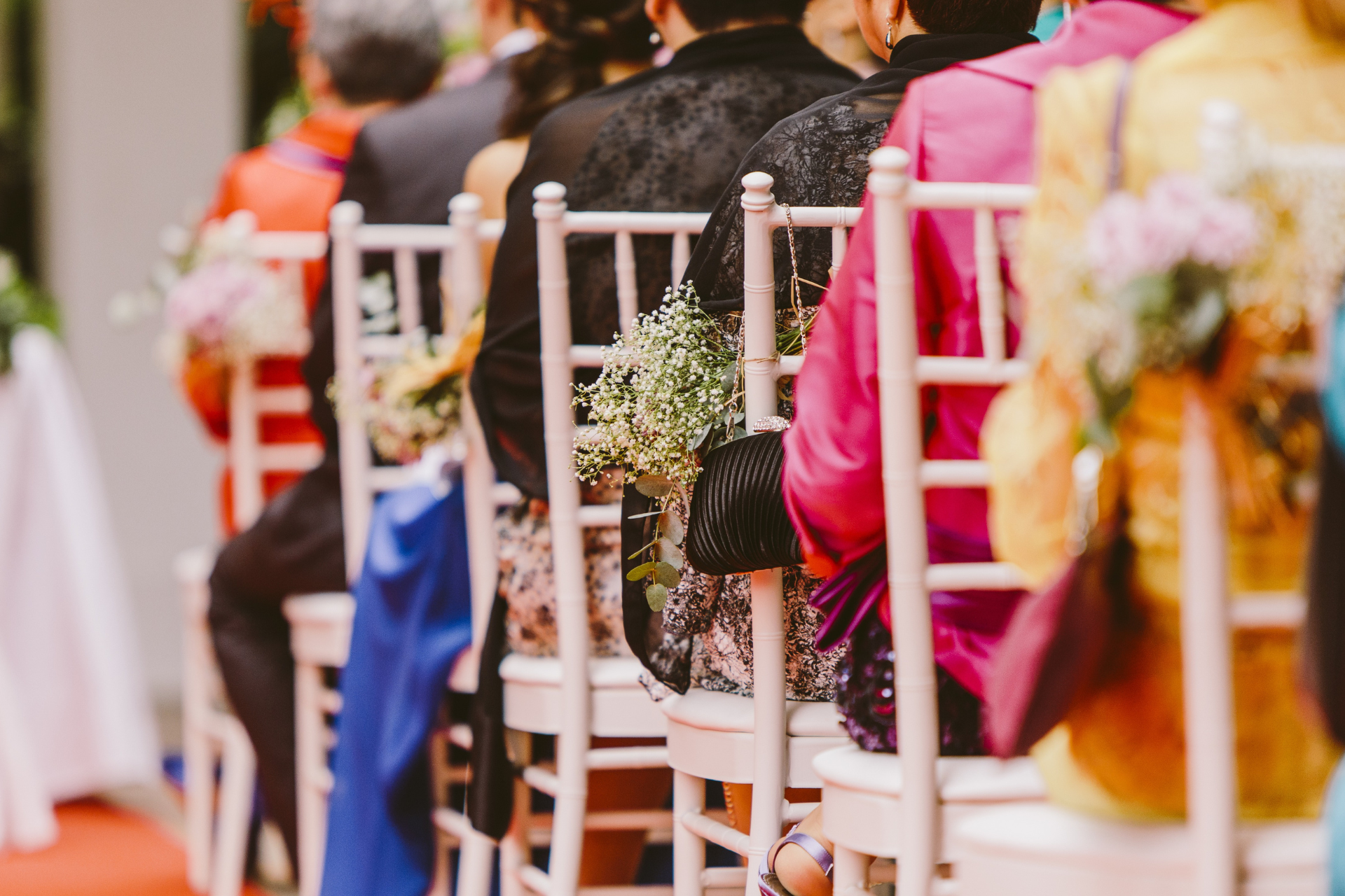 Guests seated at white chairs with colorful wraps at a decorated outdoor event