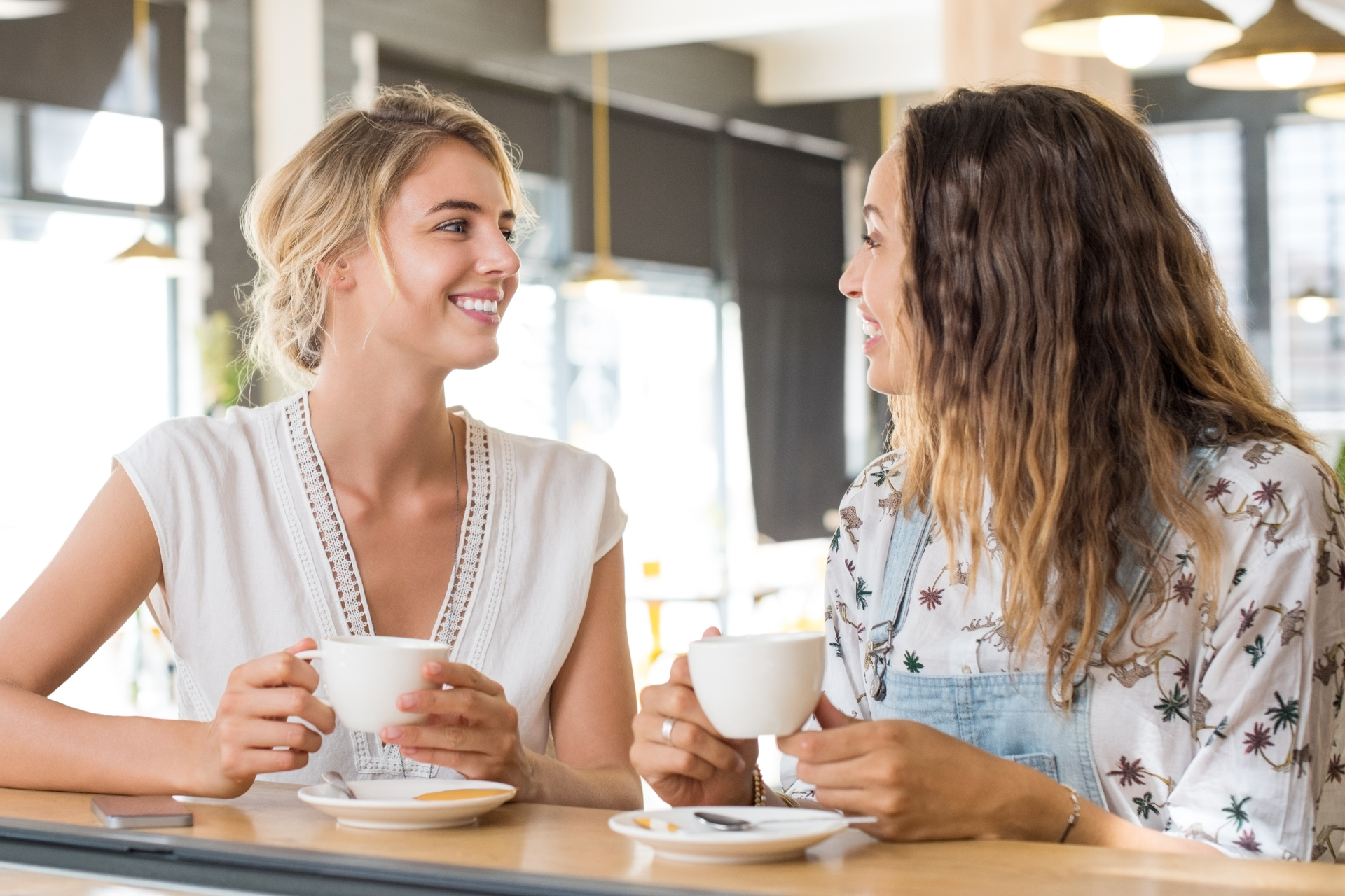 Two women smiling and chatting over coffee at a cafe table