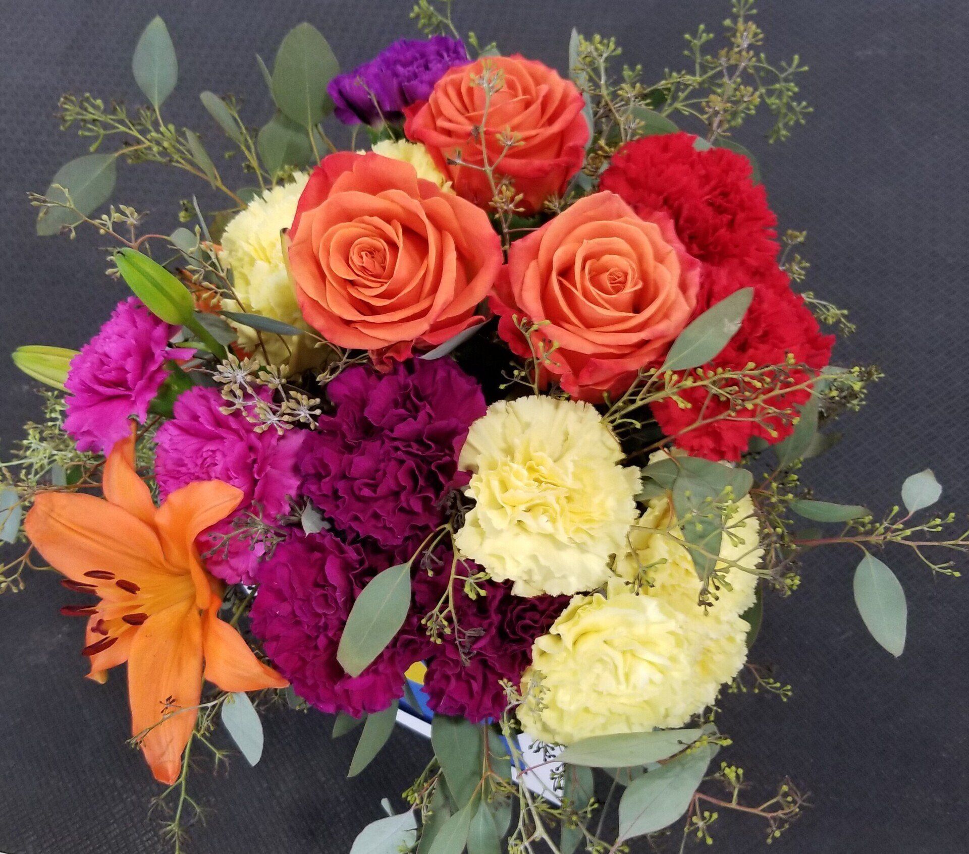 Colorful bouquet of orange roses, red carnations, yellow carnations, and purple flowers.