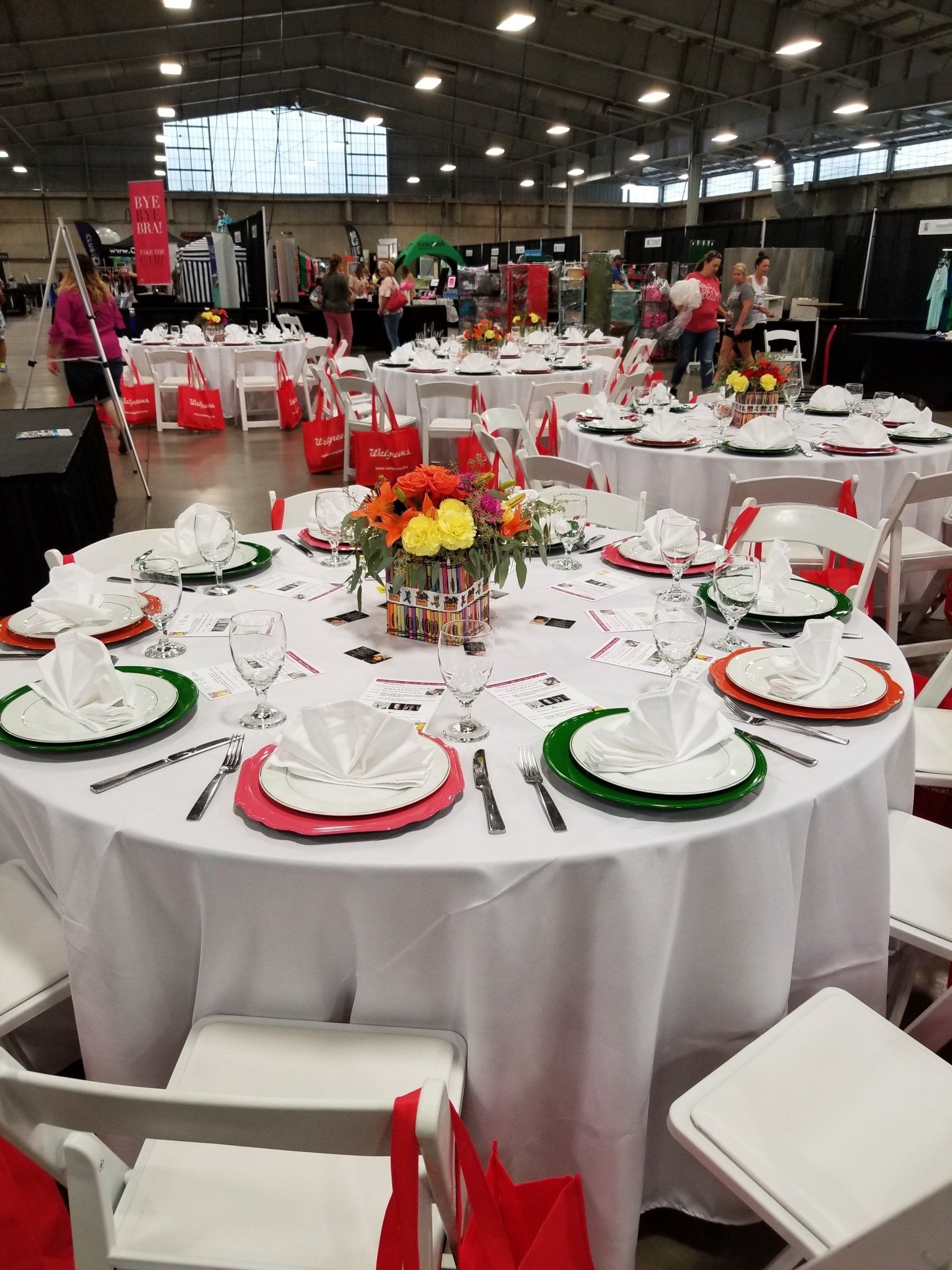 Round tables set for a party, white tablecloths, colorful place settings, flower centerpieces, indoor event.