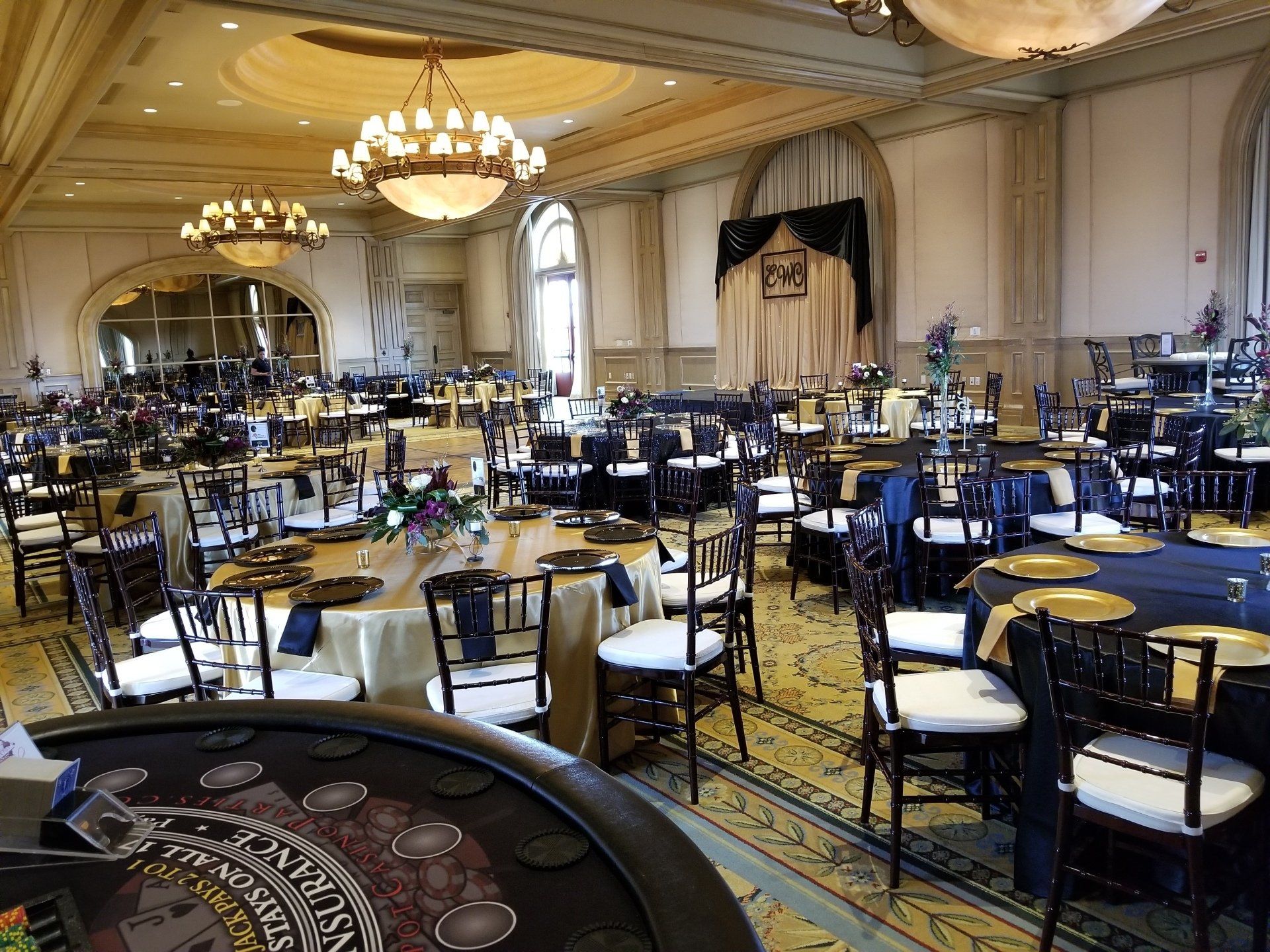 Ballroom set for an event with round tables, chairs, and chandeliers.