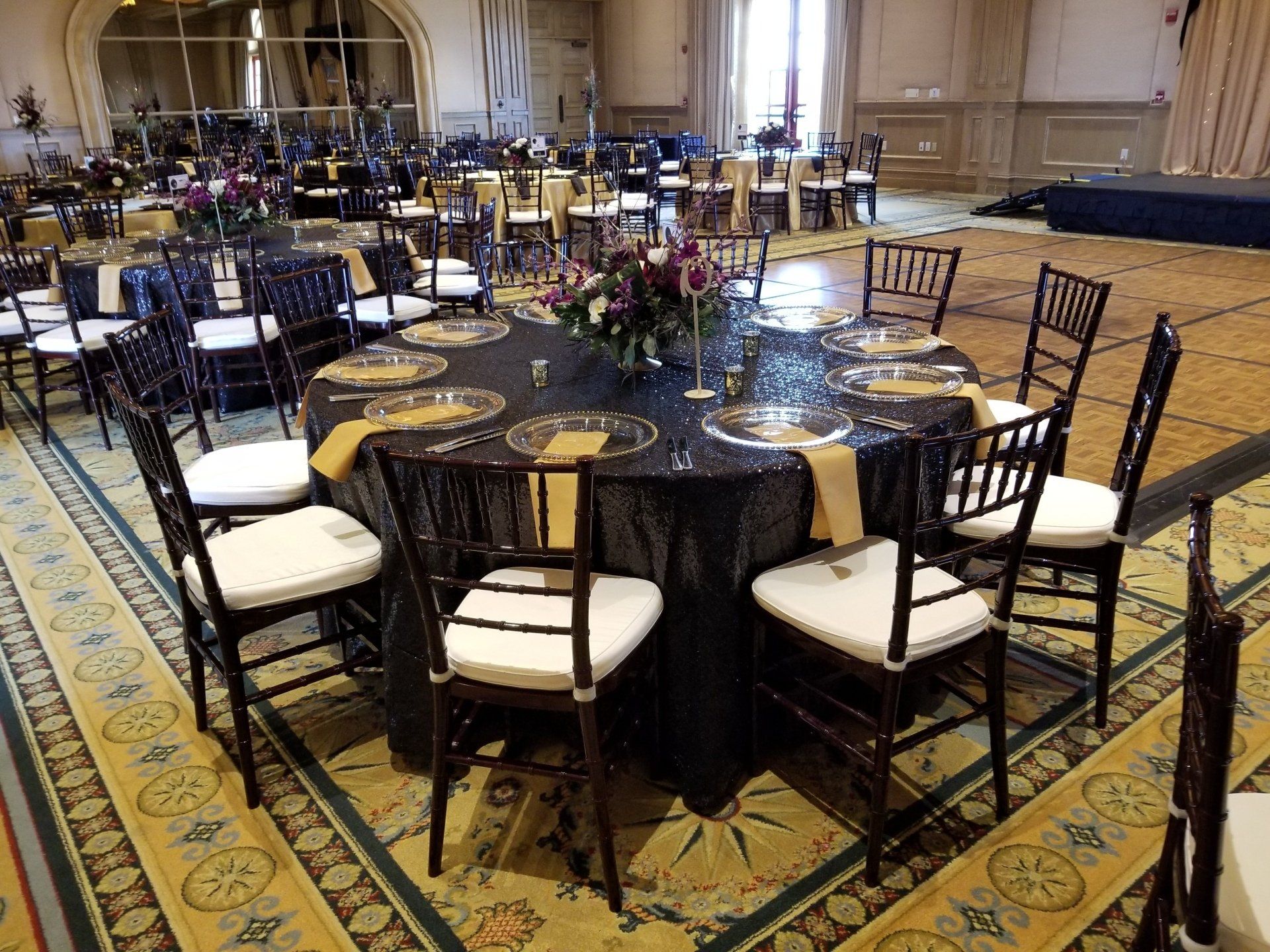 Round table set for a formal event with black tablecloth, gold accents, and chairs.