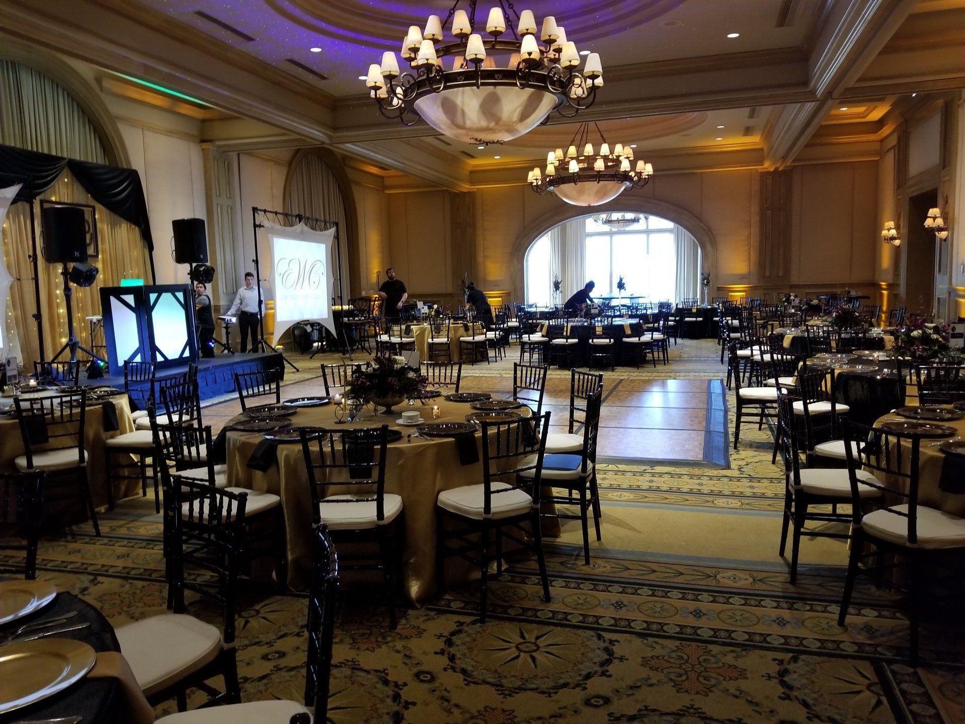 Formal banquet hall with round tables, gold tablecloths, black chairs, and a stage.