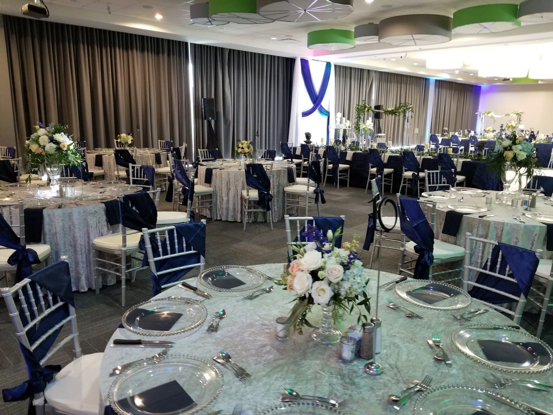 Elegant event space with round tables set for a celebration; navy and silver decor.