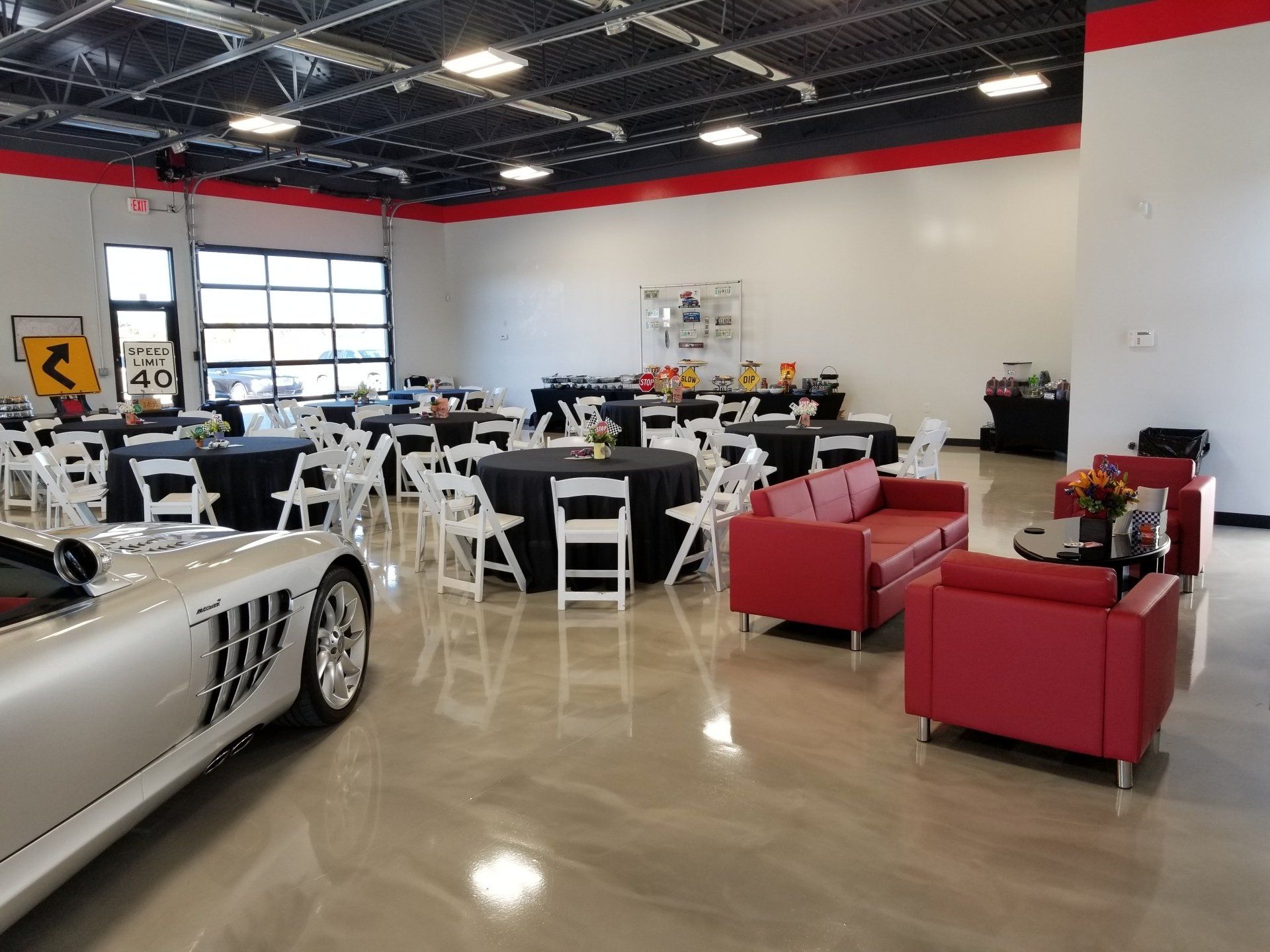 Event space with tables, chairs, and red couches; a silver sports car is visible.