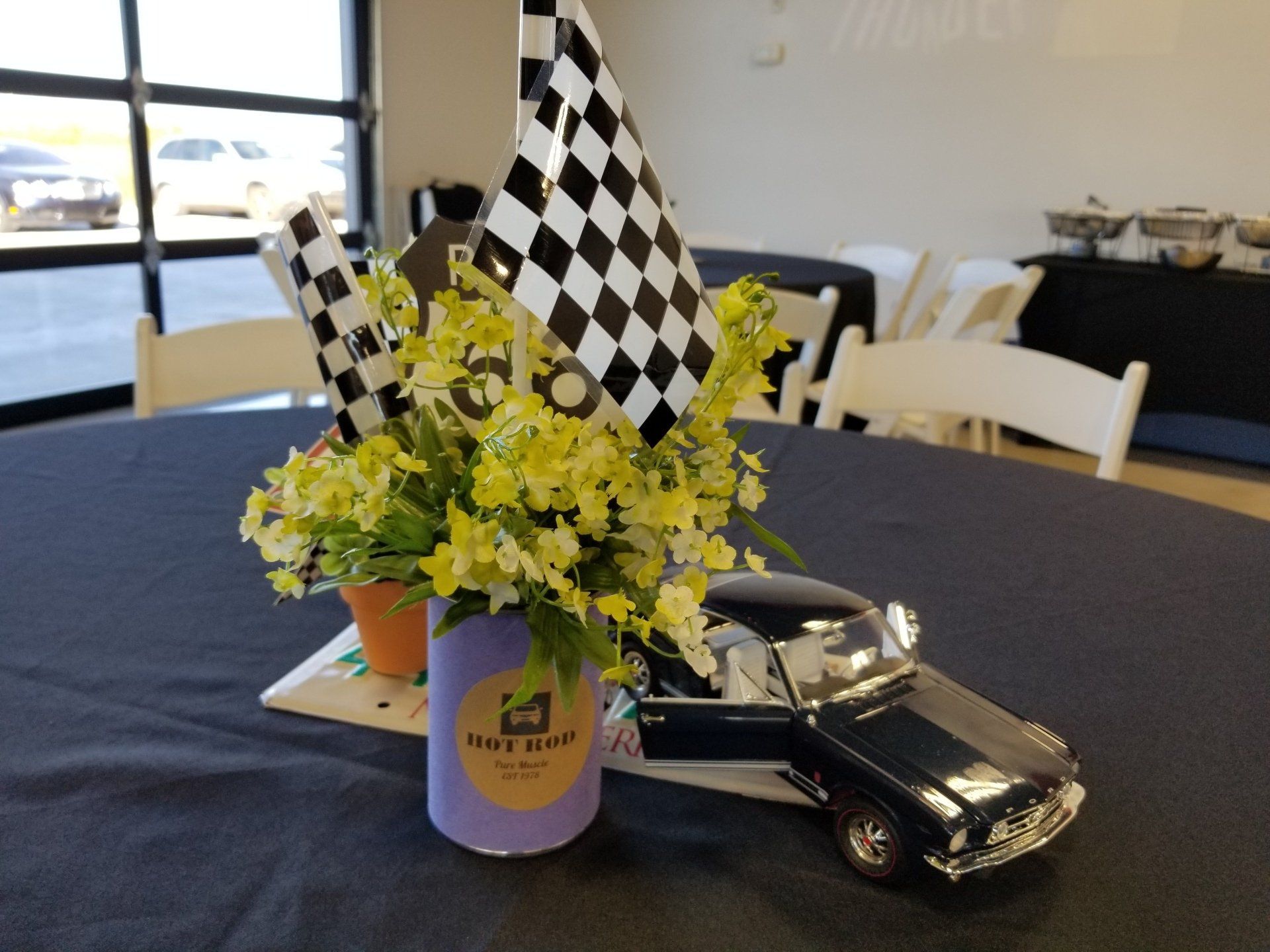 Centerpiece with a toy car, flowers, and checkered flags on a table.