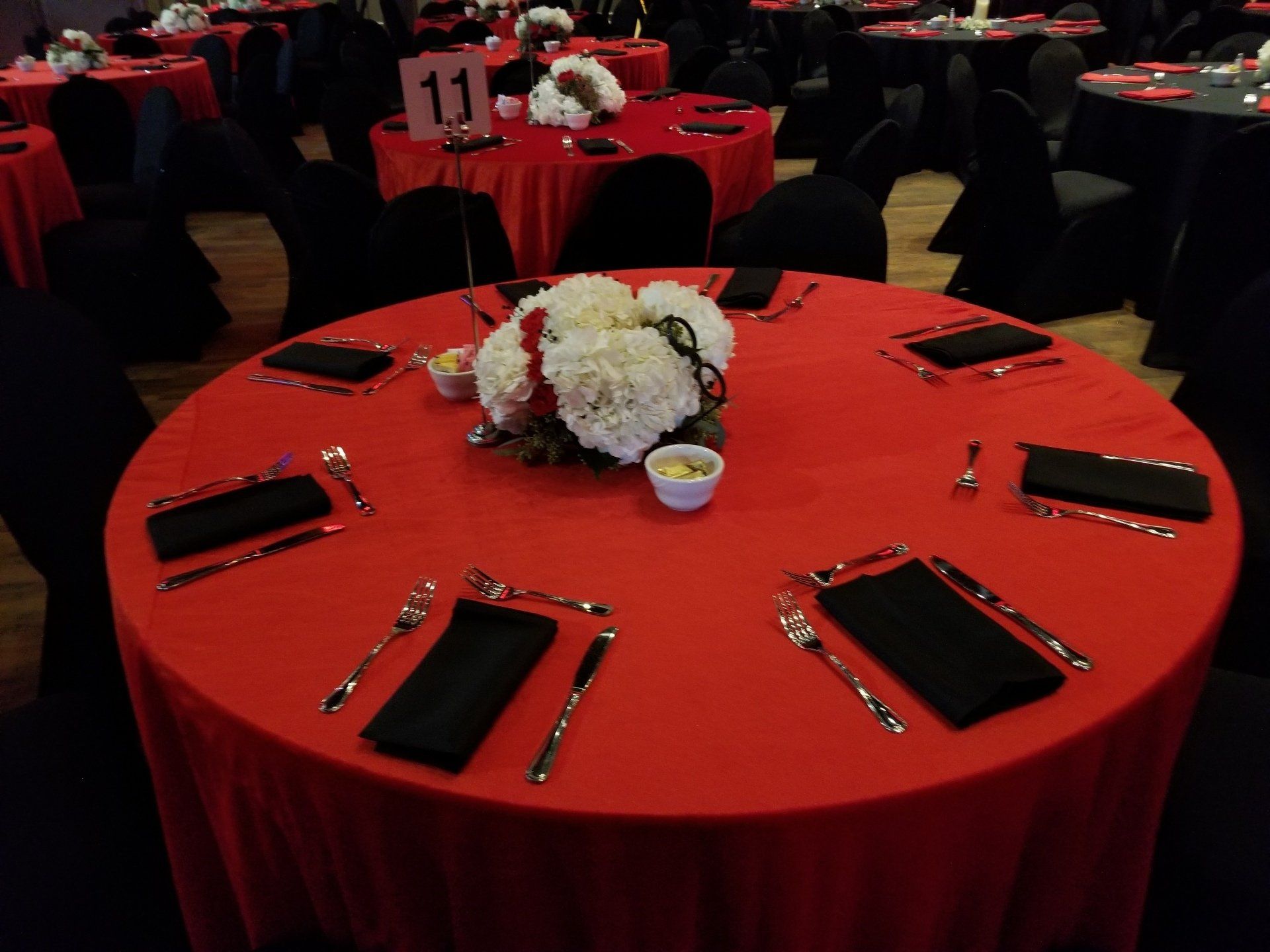 Round tables set for a formal event, red tablecloths, black napkins, white floral centerpieces.
