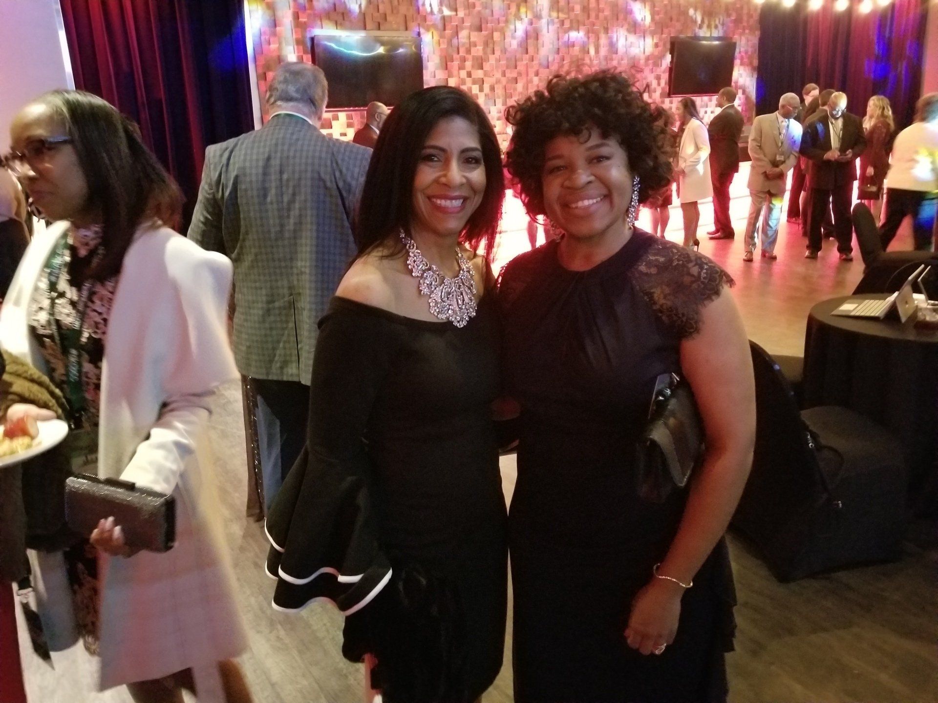 Two women in formal attire smile at the camera at an event.