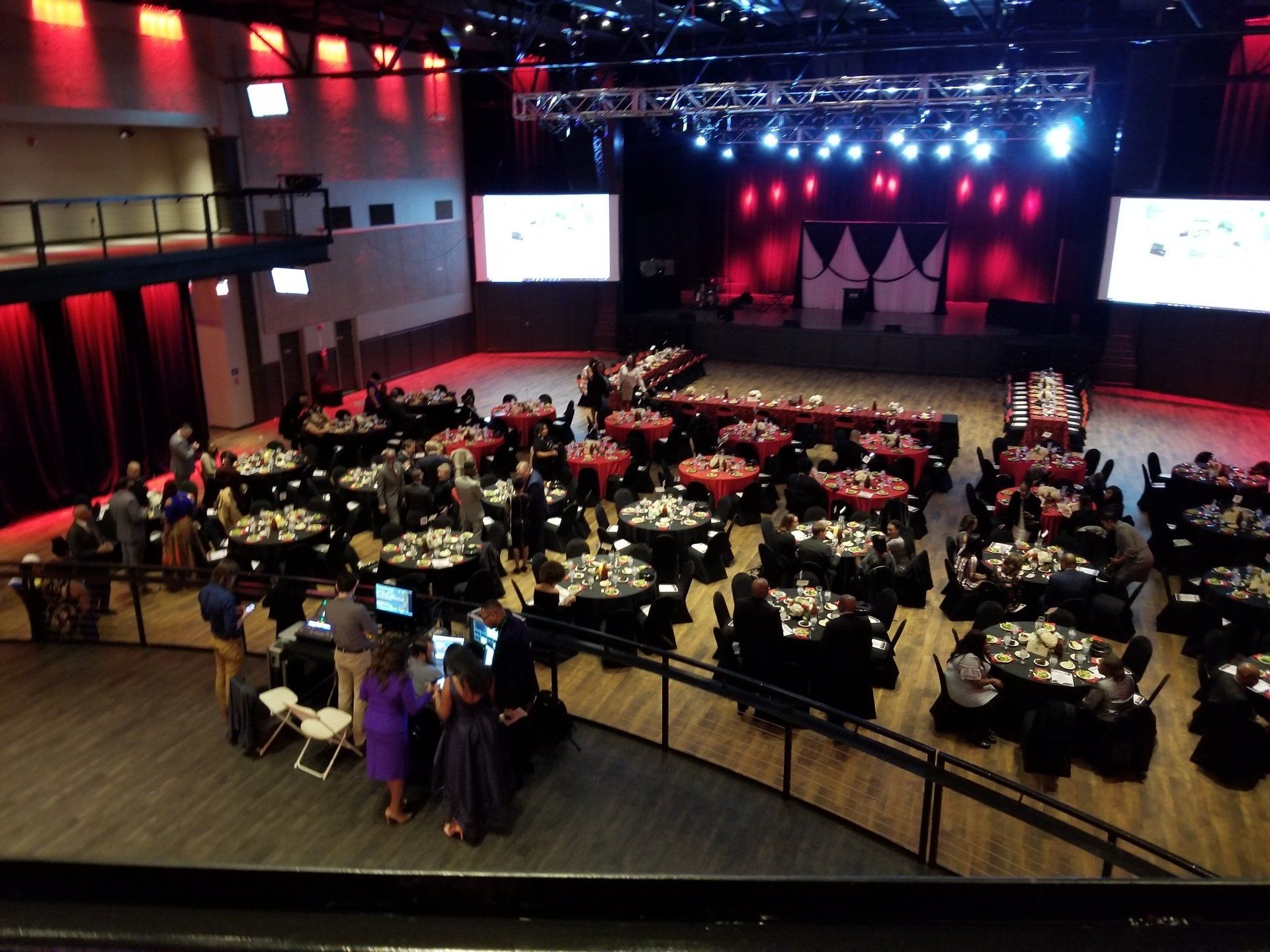 Large event space with tables set for a banquet. Stage with lights and screens at the back.