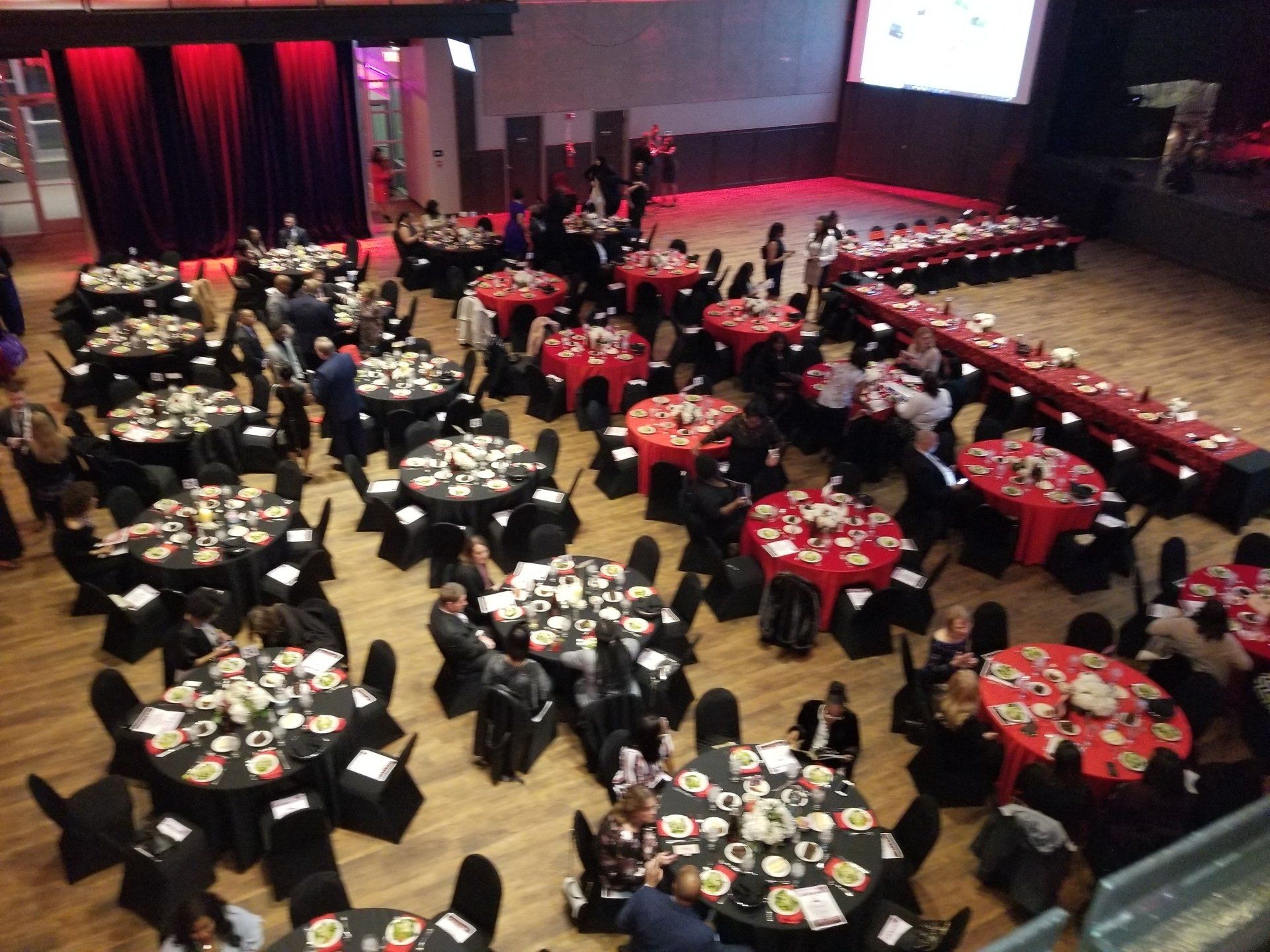 Large banquet hall with round tables set for a formal event; some tables have red tablecloths, others black.