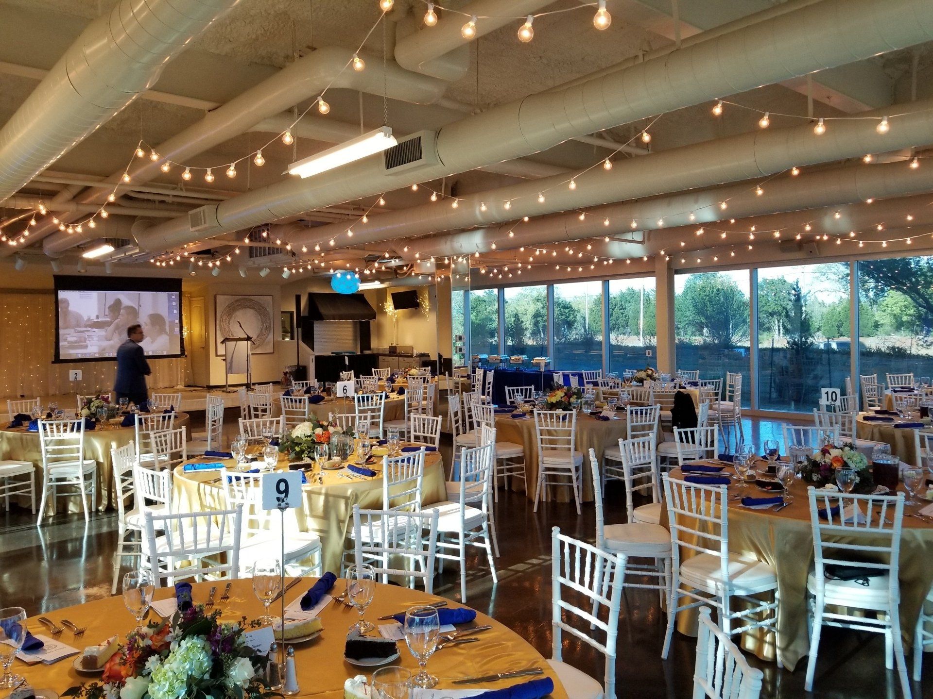 Banquet hall with tables set for a formal event. String lights hang from the ceiling.
