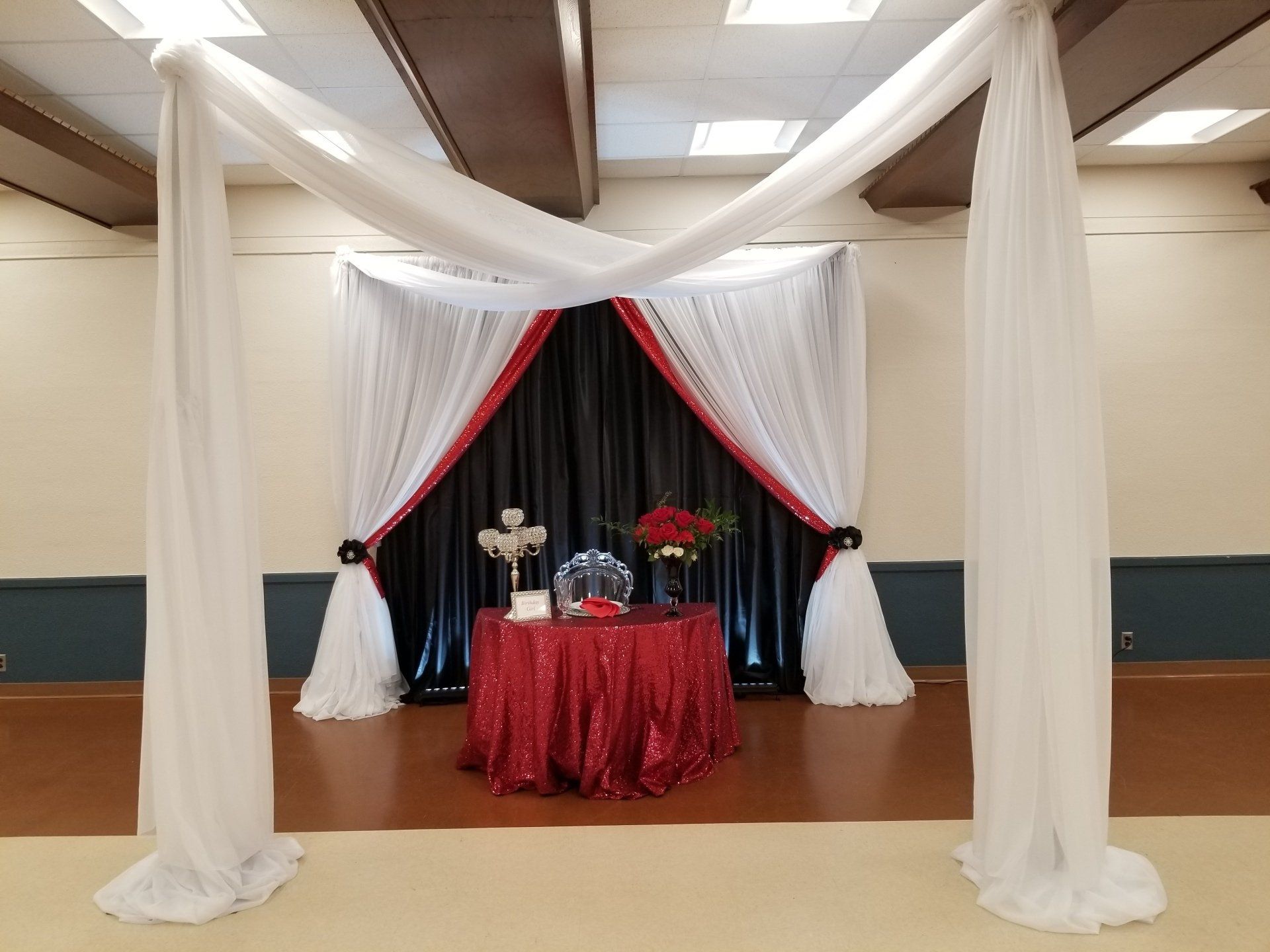 Wedding reception backdrop: White draping frame with red and black curtains, red sequined table, and floral arrangements.