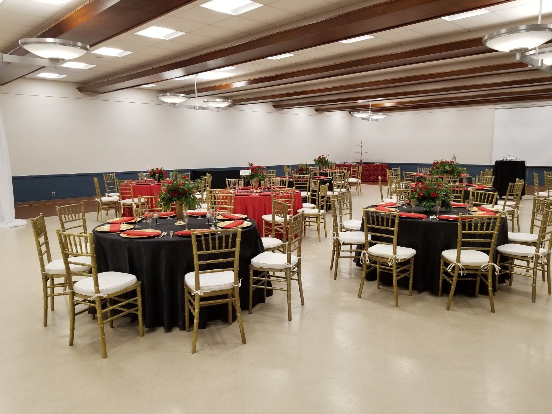 Reception hall with round tables covered in red and black cloths, gold chairs.