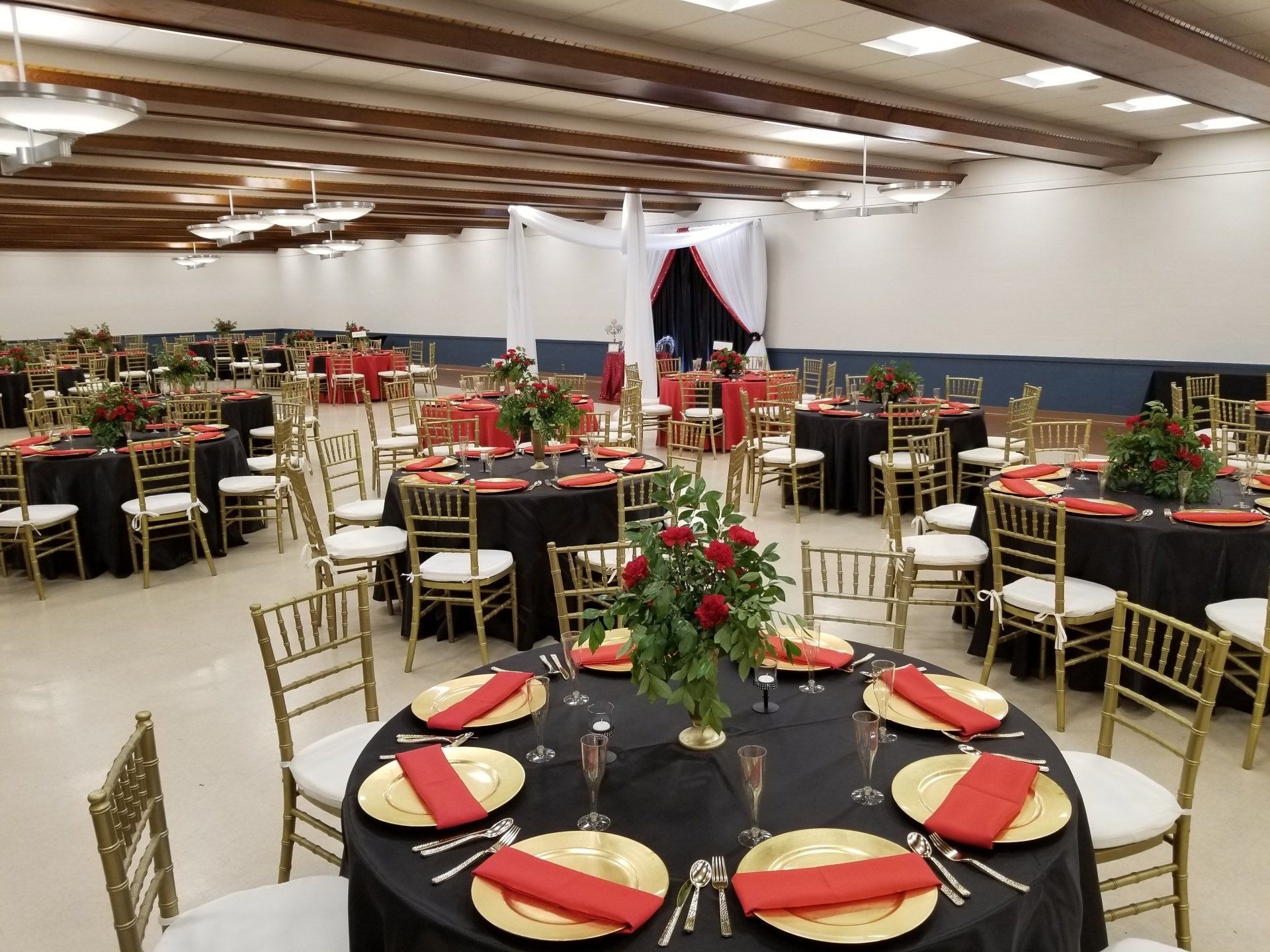Formal event space with round tables set with black tablecloths, gold chargers, and red napkins.