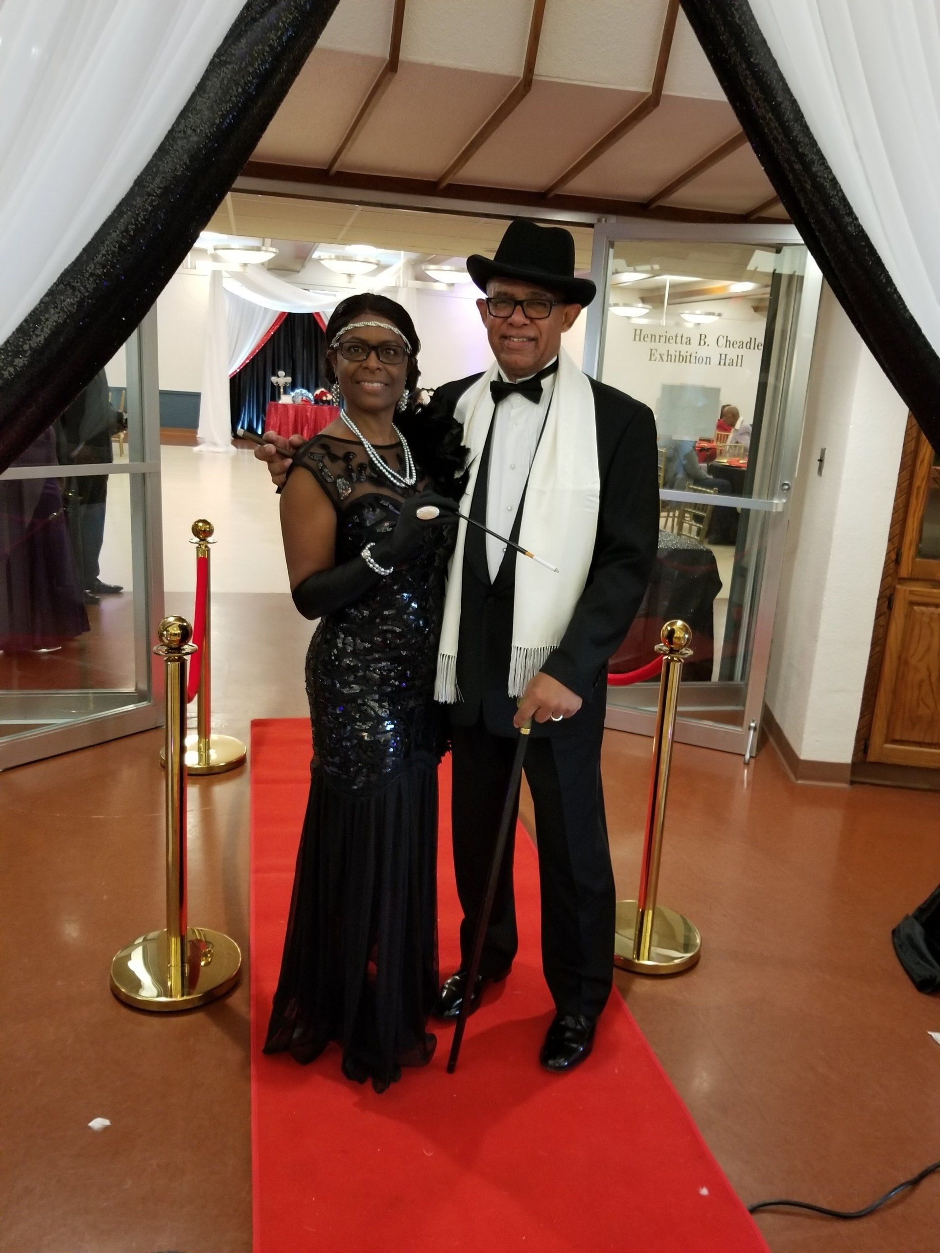 Couple in formal attire pose on red carpet, black and white color scheme.