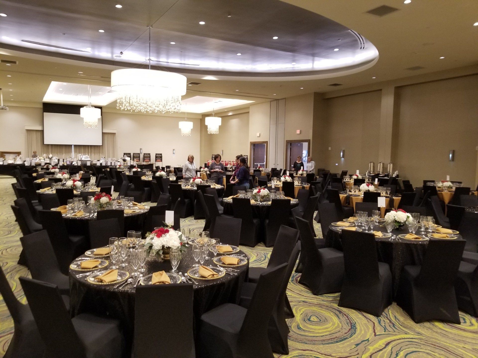 Banquet hall set for event; round tables with black linens, centerpieces, and place settings.