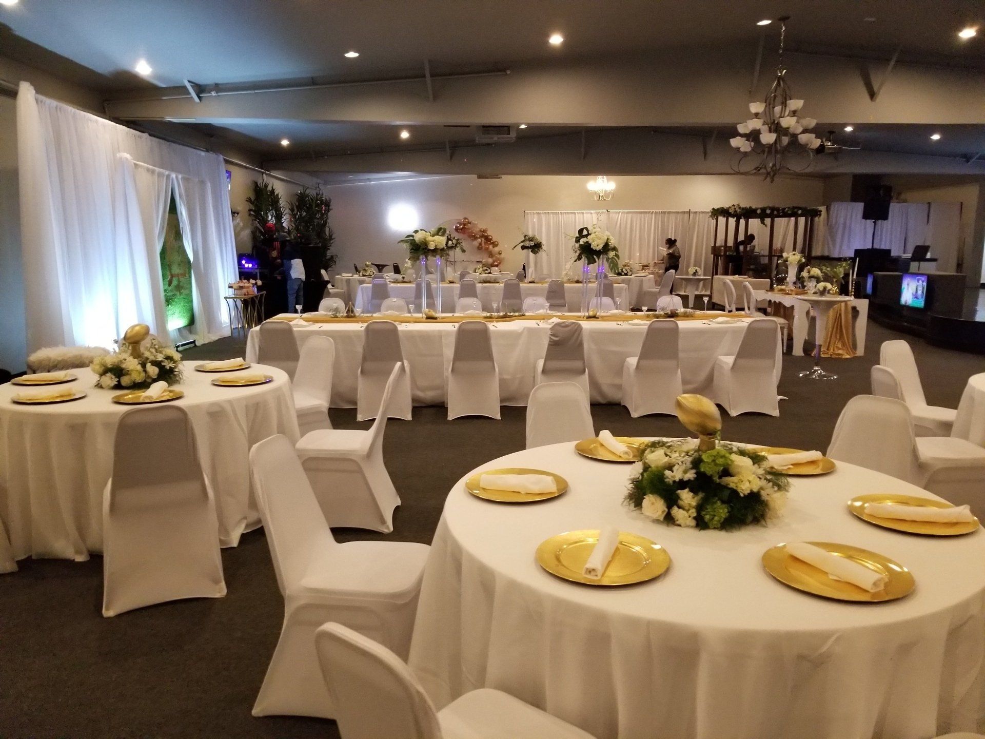 Wedding reception hall with round and rectangular tables, draped in white linens and decorated with floral centerpieces.