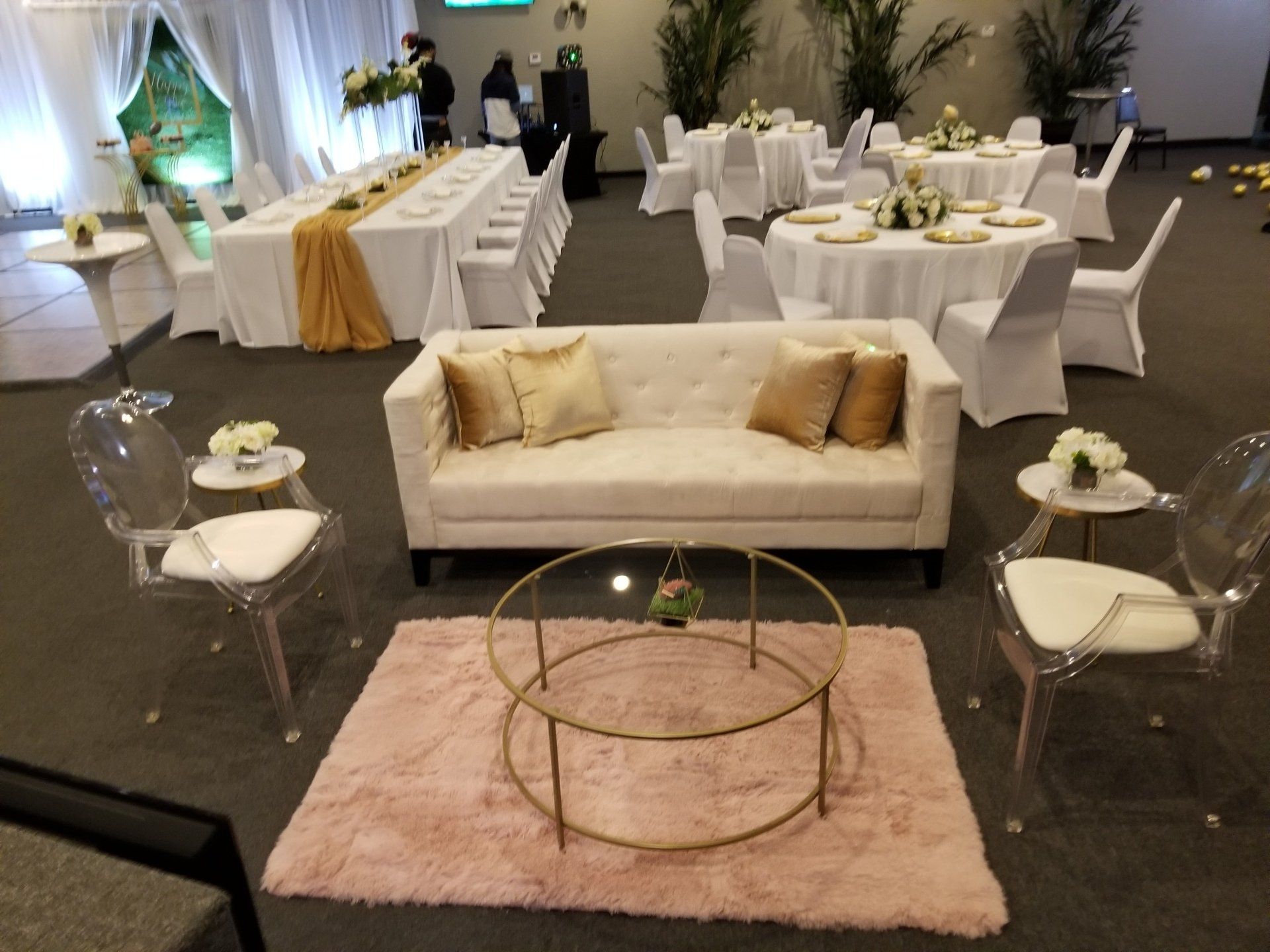 Event space with a cream-colored couch, round coffee table, and acrylic chairs; tables set for guests.
