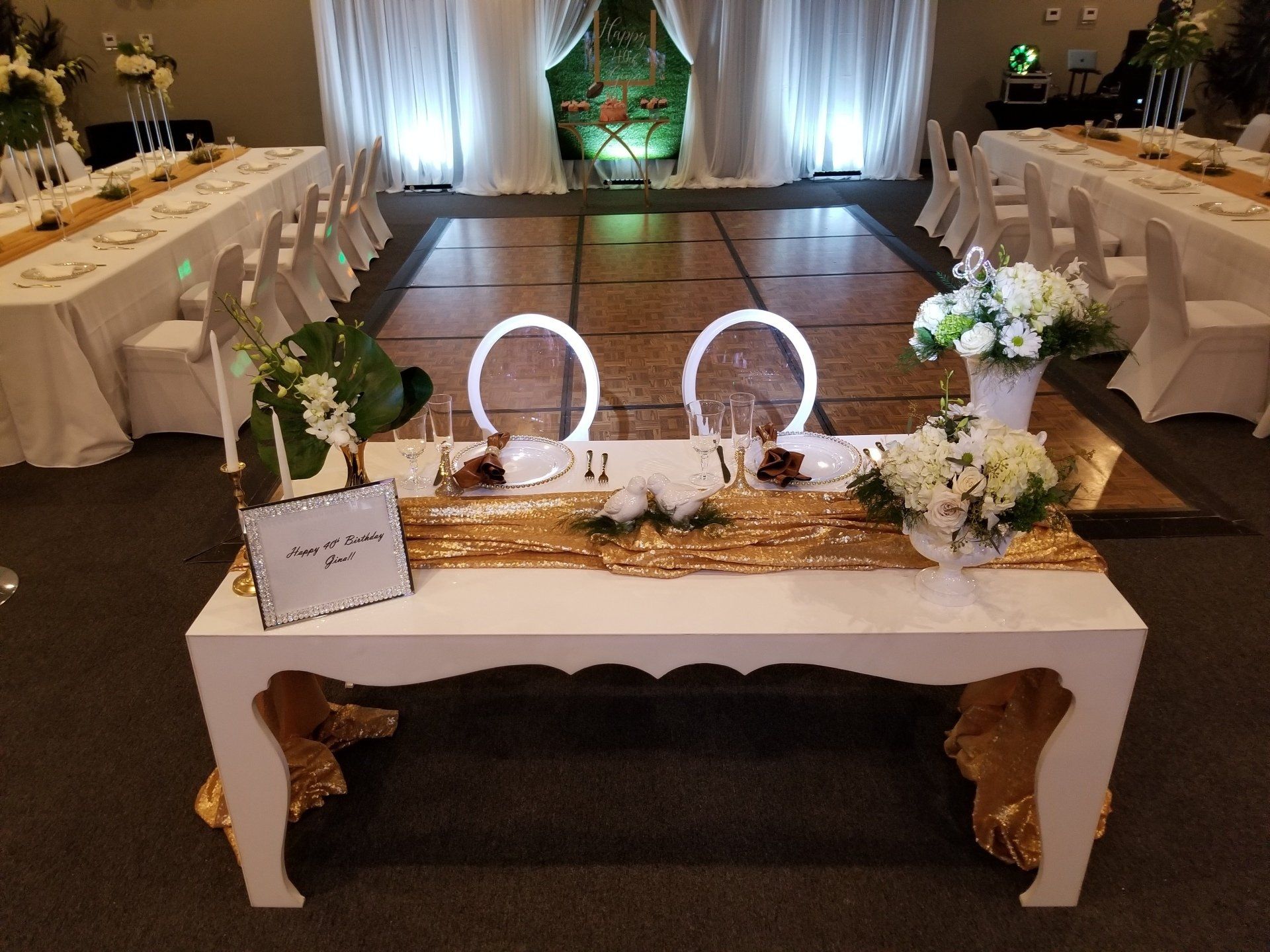 Wedding reception with a white sweetheart table, gold accents, and a dance floor.