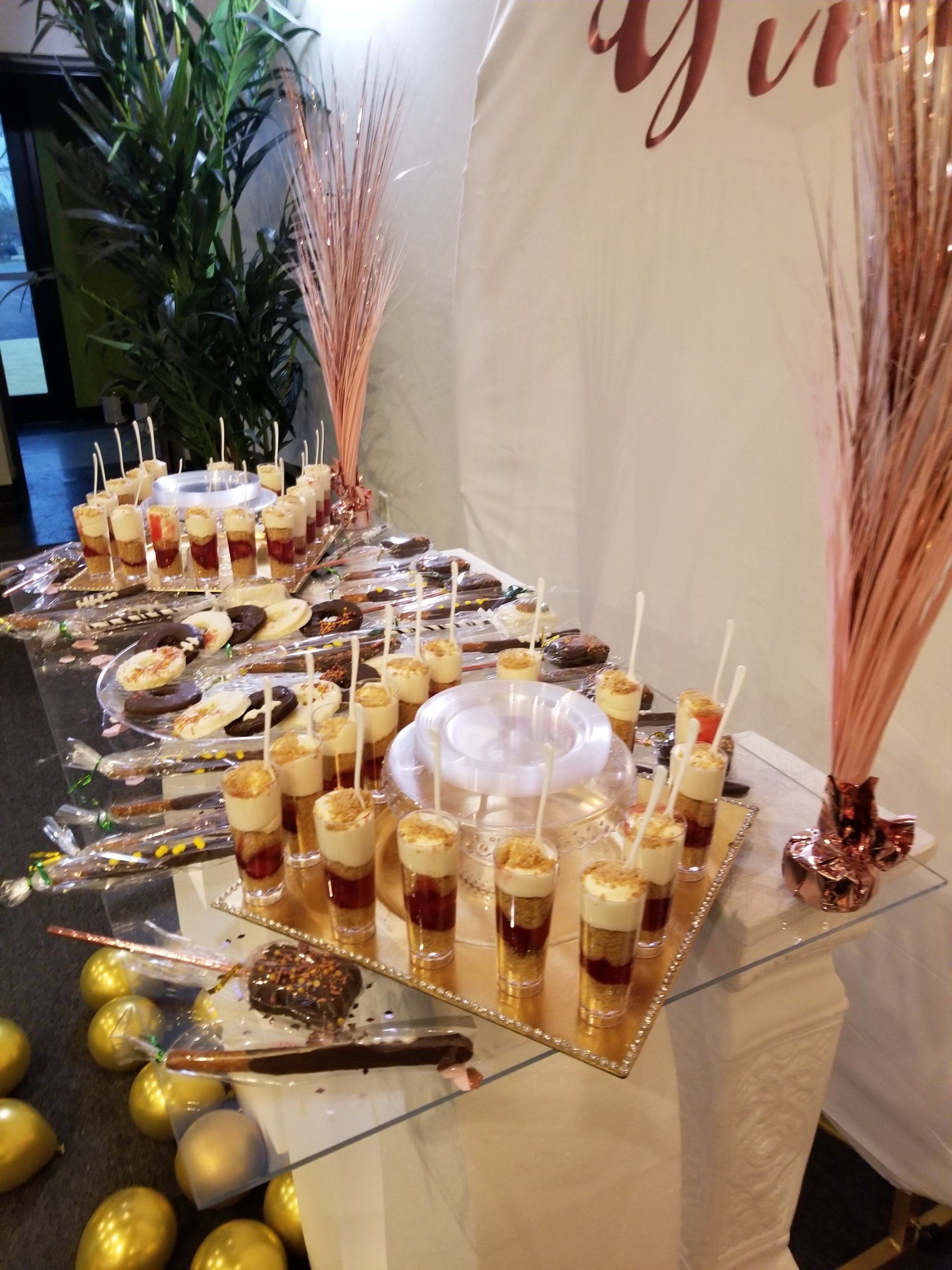 Dessert table with various treats arranged on mirrored surfaces, decorated with gold and pink accents.