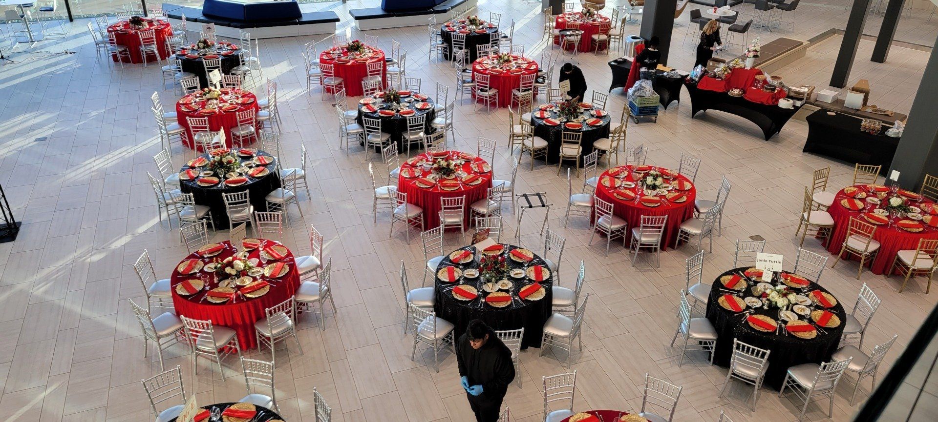 Tables set for a formal event in a large, open space with red and black tablecloths.