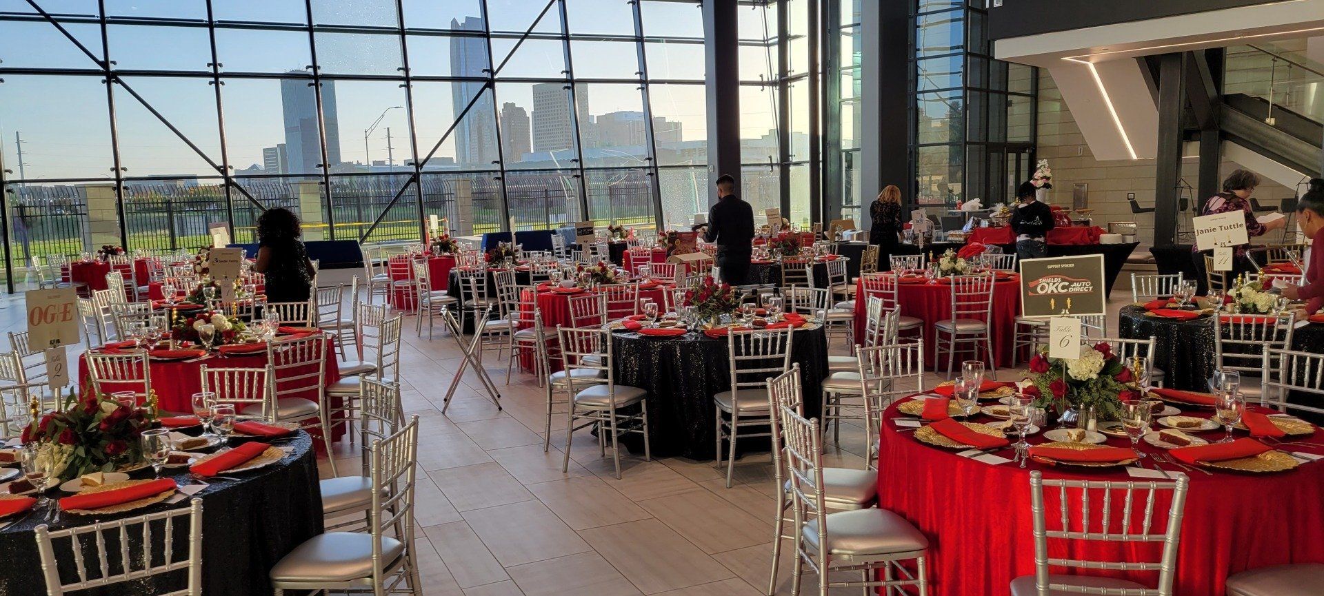 An event space with tables set for a party, looking out at a city skyline through large windows.