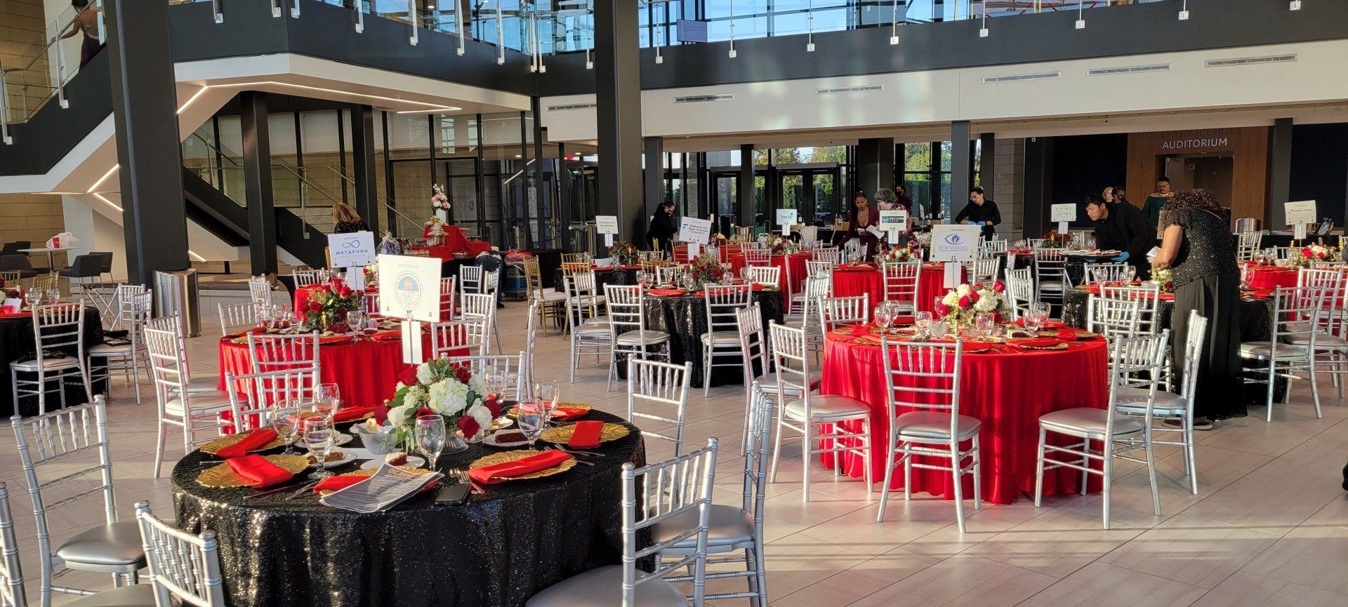 A large event hall with round tables covered in red and black tablecloths, with white chairs.