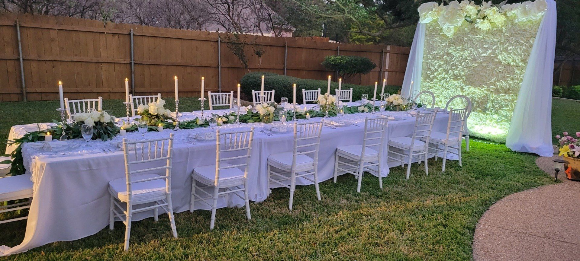Outdoor wedding reception table set with white linens, flowers, and candles.