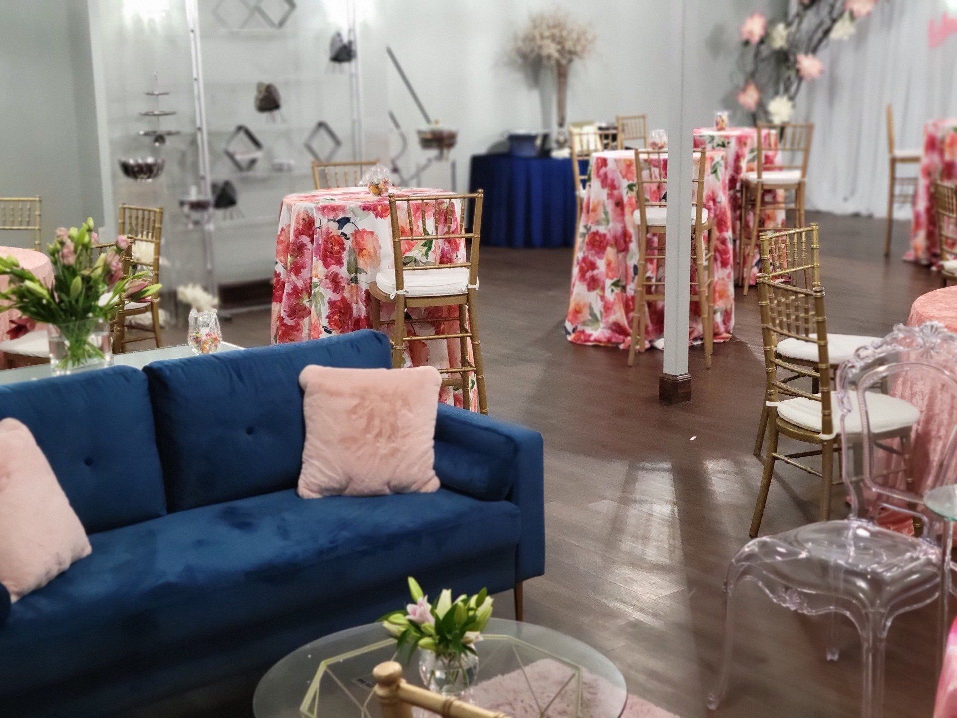 Event space with floral print tables, blue sofa, and clear and gold chairs.