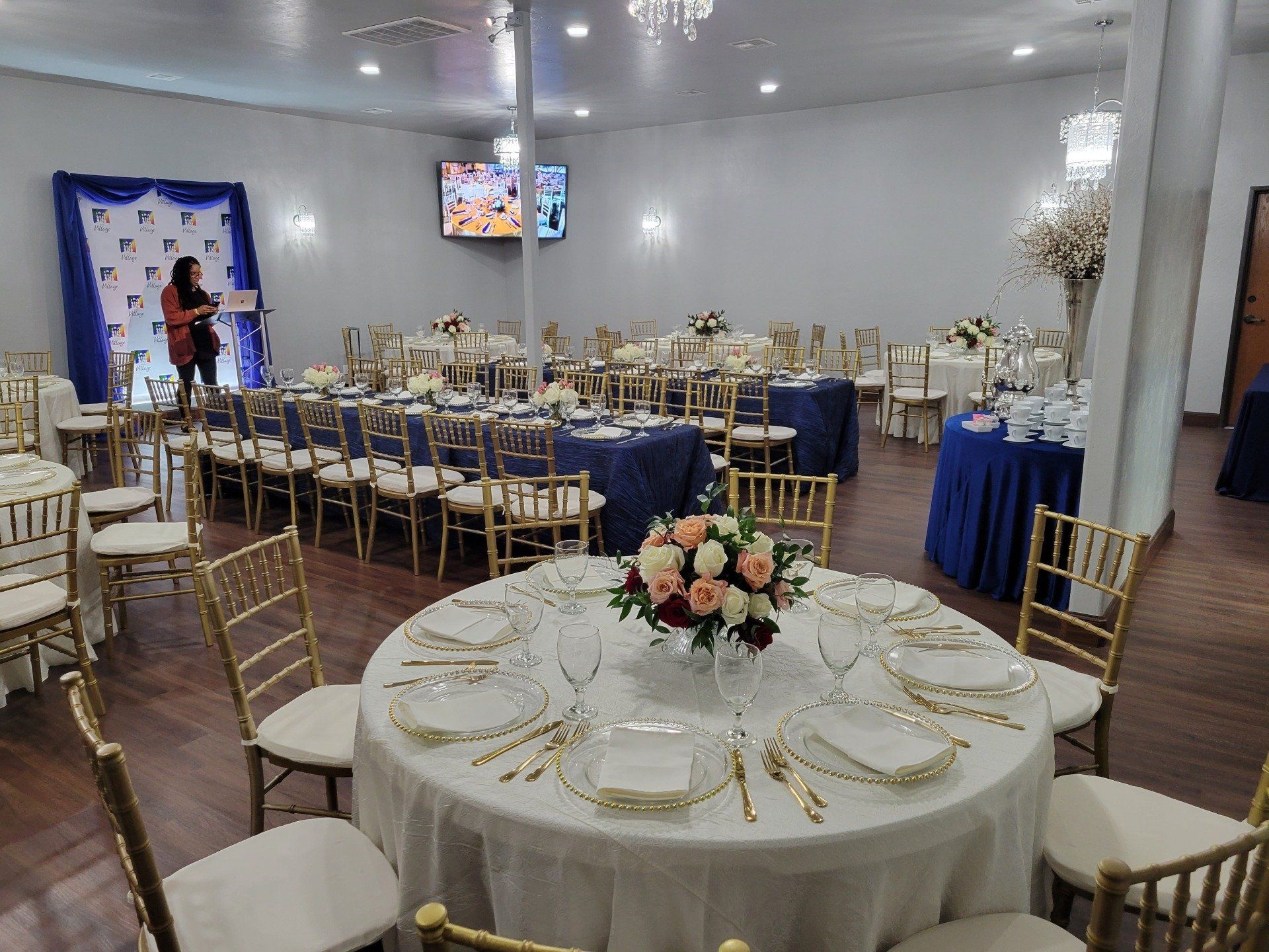 Banquet hall with tables set for a formal event; a woman speaks at a podium.