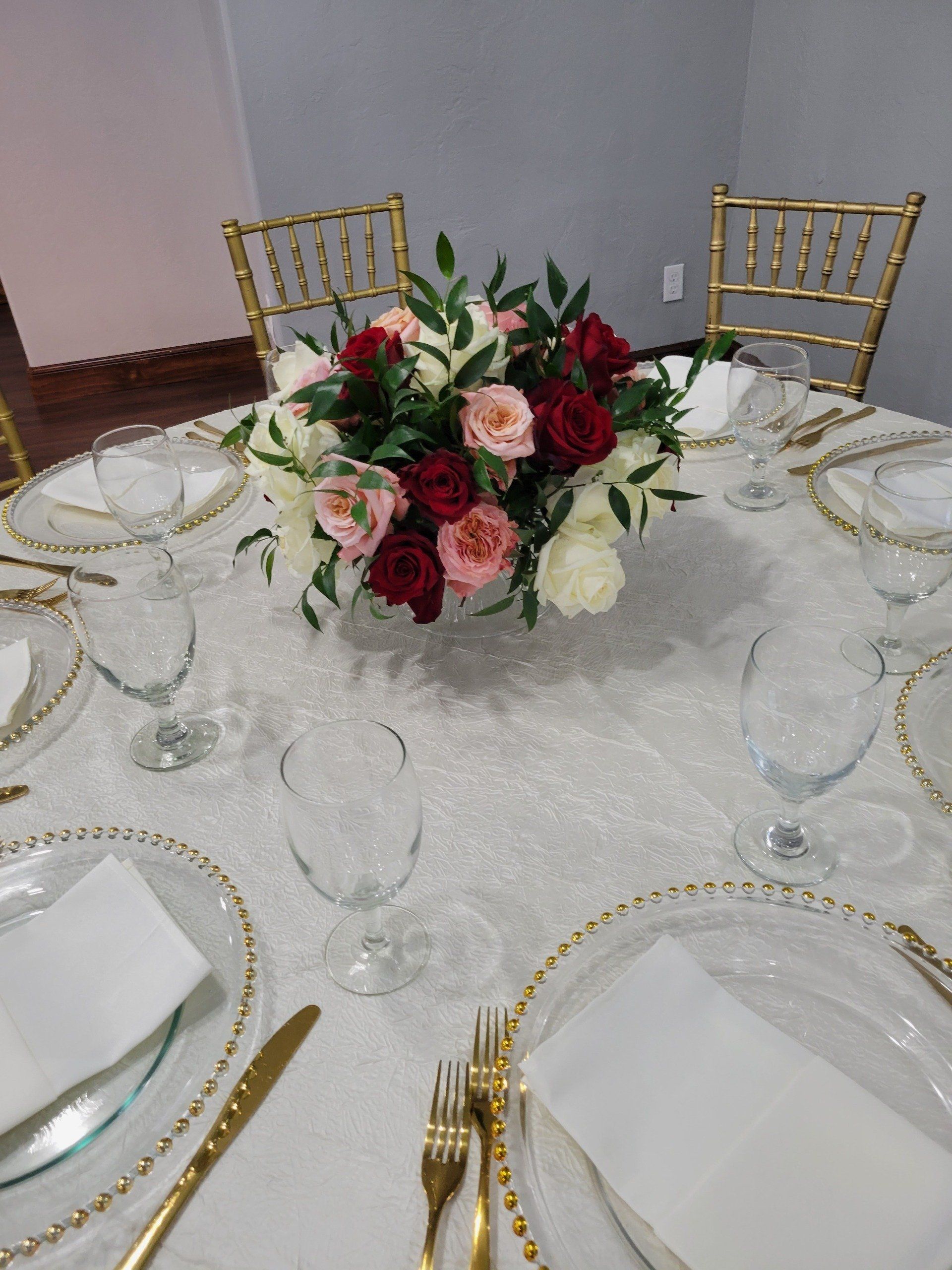 Round table set for a formal event, featuring a floral centerpiece, gold accents, and place settings.